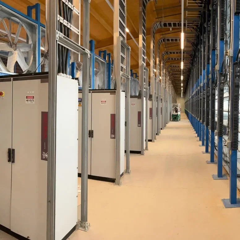 Industrial data center or server room with cabinets, cooling fans, and overhead lighting.