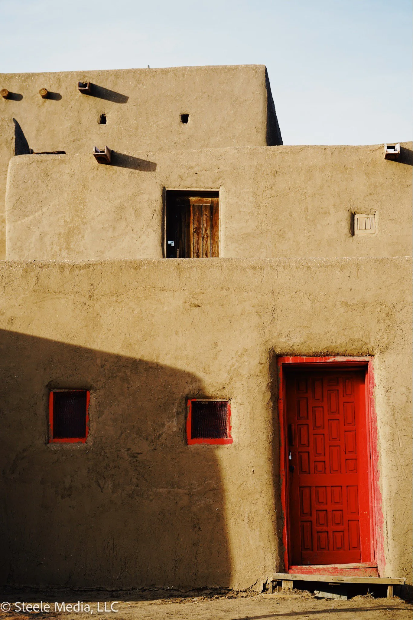 Adobe style adobe building with a red door and small red windows, featuring traditional Native American architecture in a desert setting.