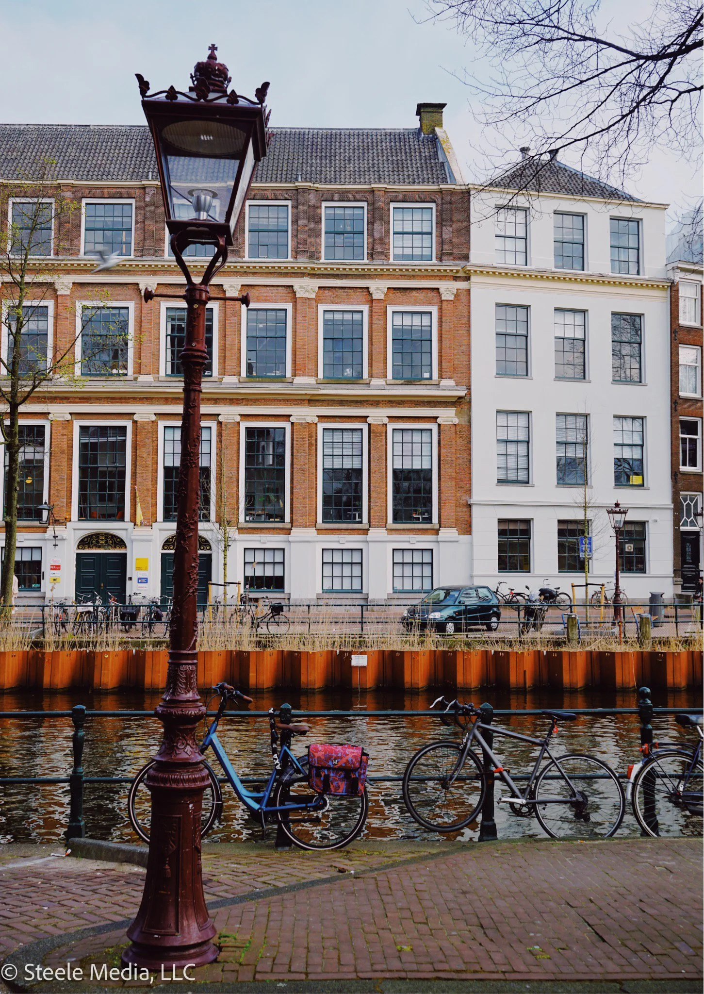 A canal with a decorative street lamp and bikes parked along the edge, with historic brick and white buildings across the water in the background.