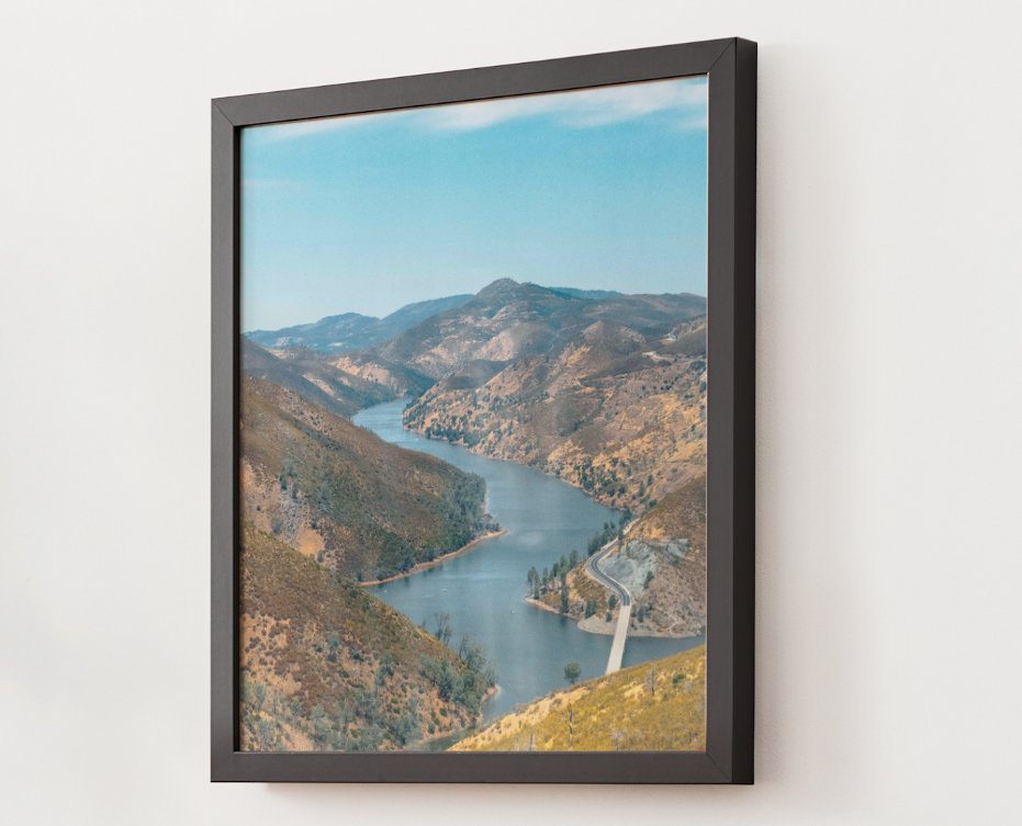 Framed landscape photo of a winding river flowing through hills and mountains under a blue sky.