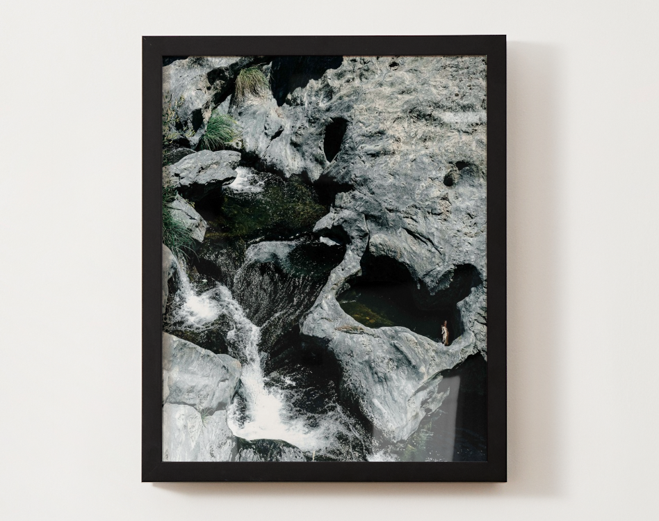 Photograph of rocky river with small waterfalls and streams, framed and hung on a white wall.