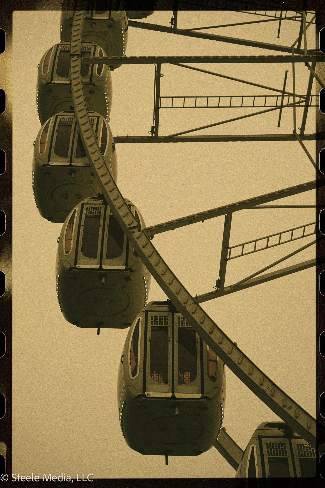 Close-up of a Ferris wheel with four enclosed cabins seen from below against a cloudy sky.