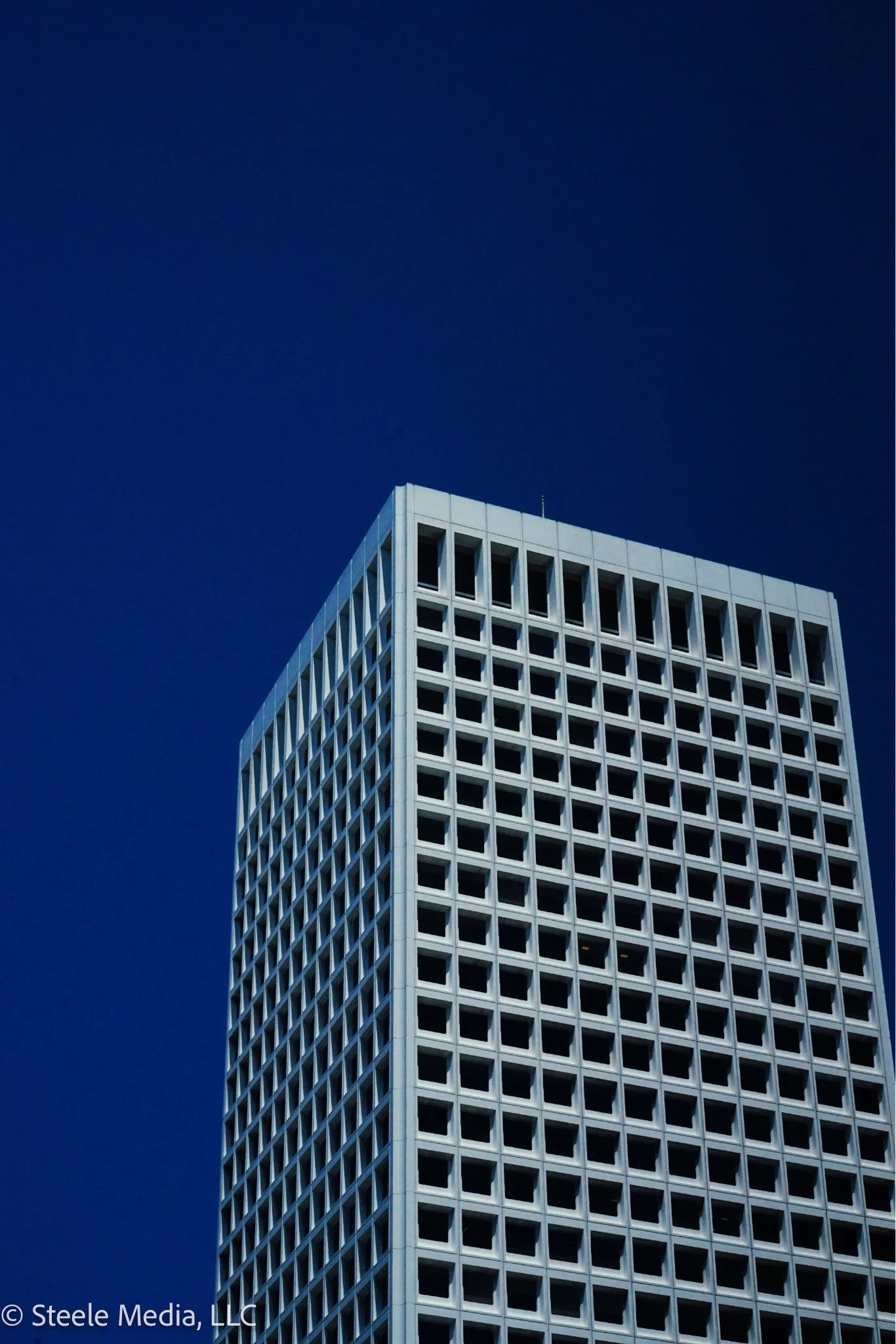 A tall skyscraper with a grid of square windows against a clear dark blue sky.