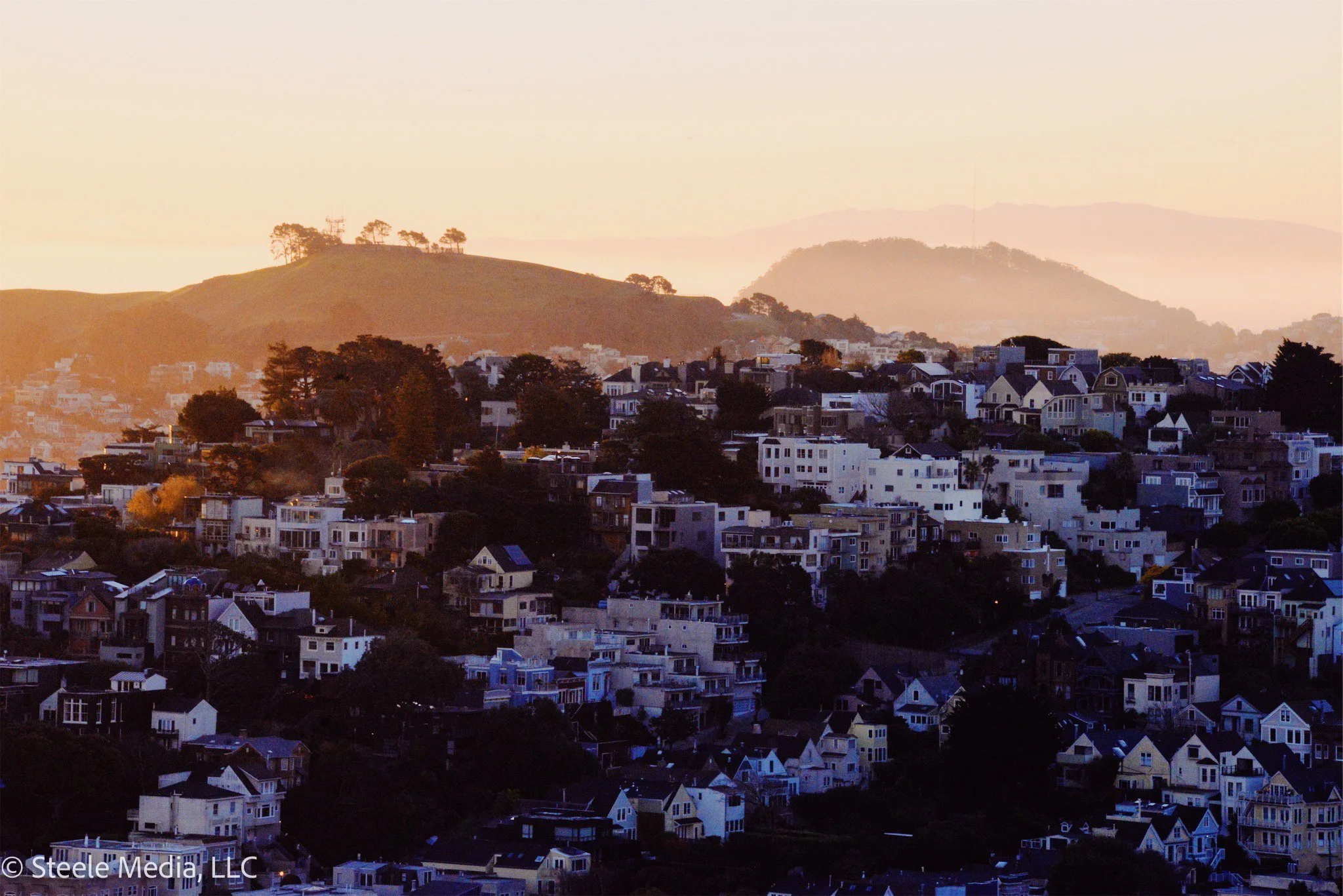 Hilly neighborhood with many multi-story houses on a hillside during sunset or sunrise.