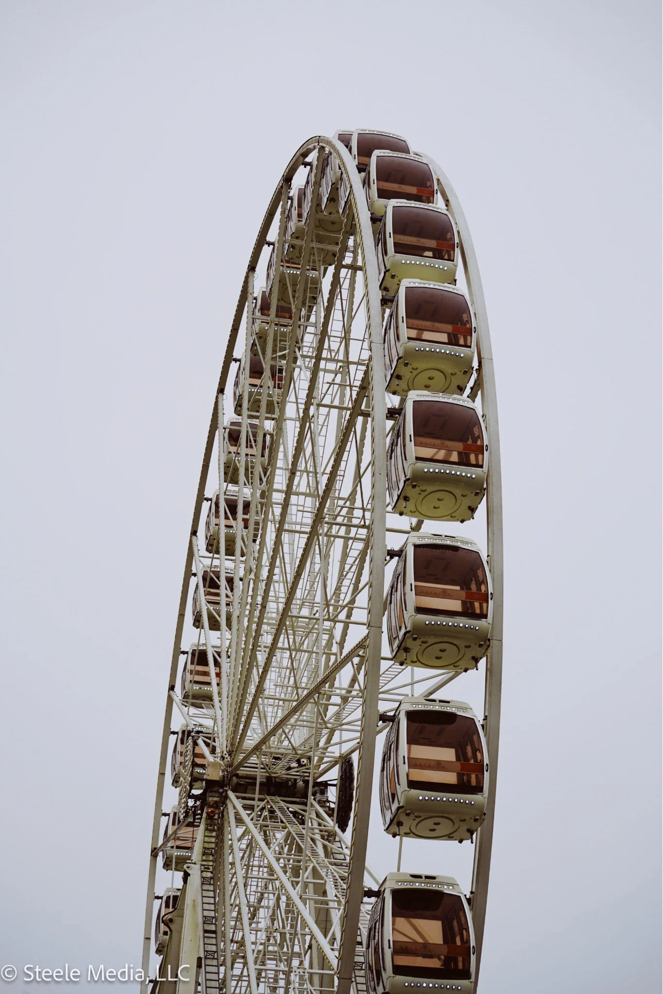 A large Ferris wheel with enclosed gondolas against a gray sky.