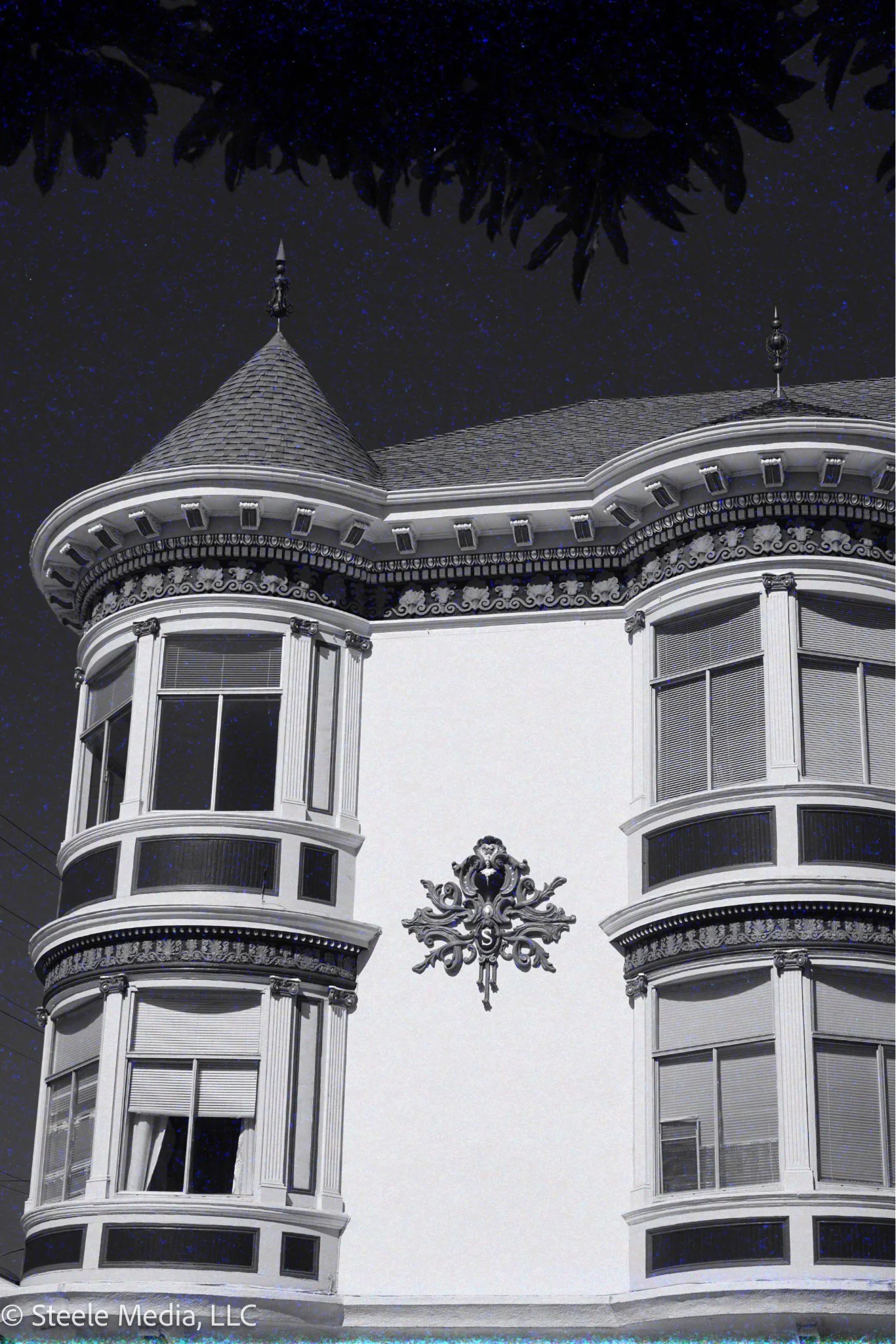 Night view of an ornate Victorian-style house with a turret, bay windows, and decorative trim, under a starry sky.