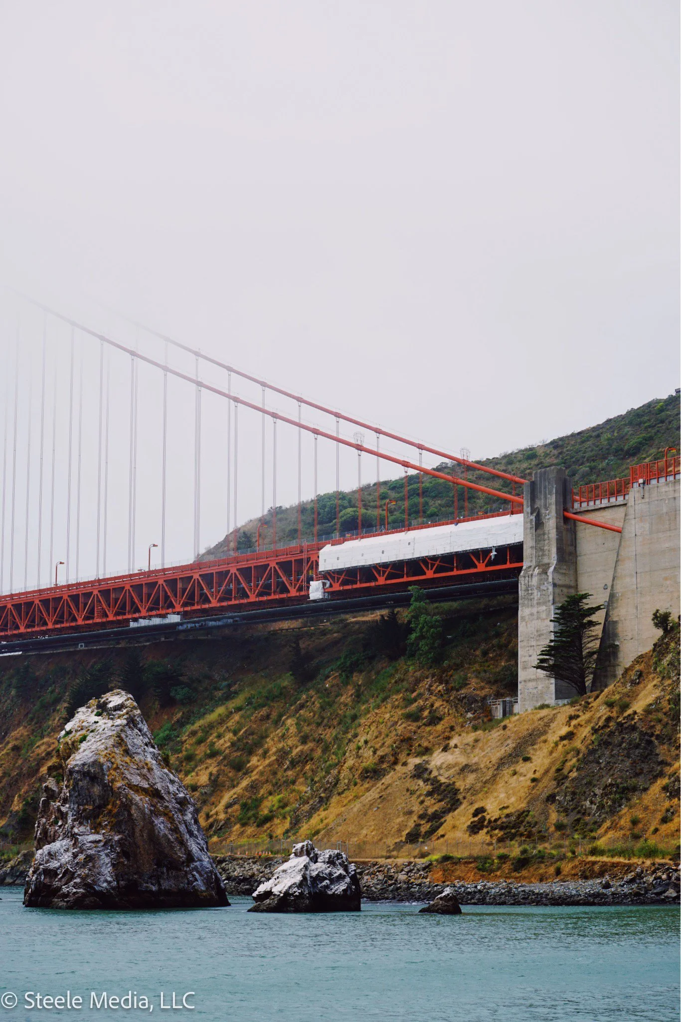 A view of the Golden Gate Bridge with foggy skies over the water and rocky shoreline below.