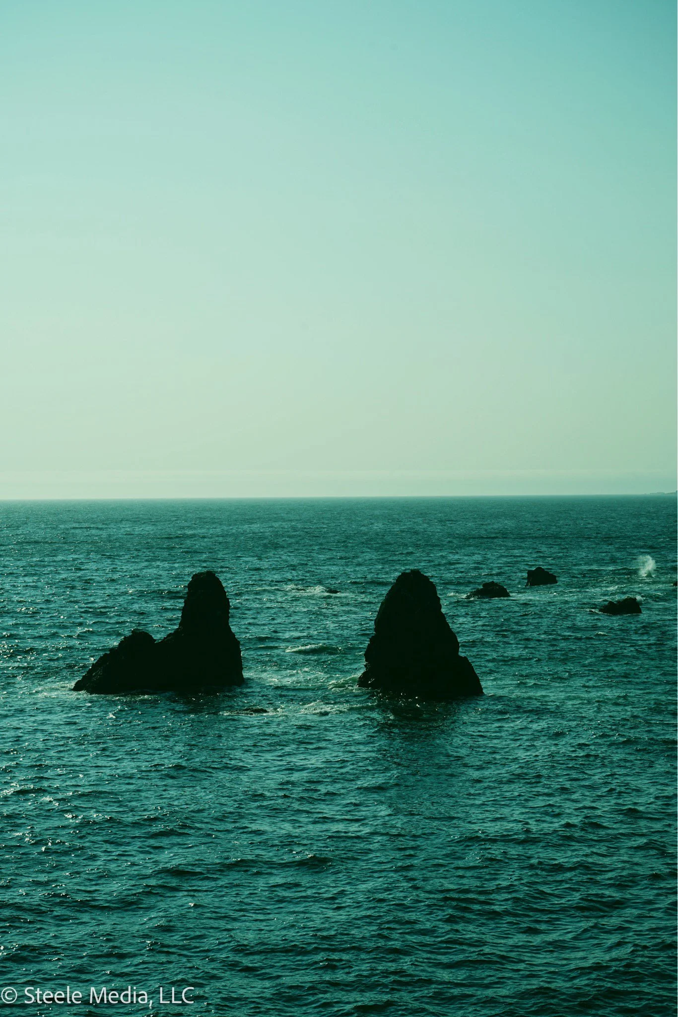 Ocean with seven large dark rock formations in the water, under a pale sky.