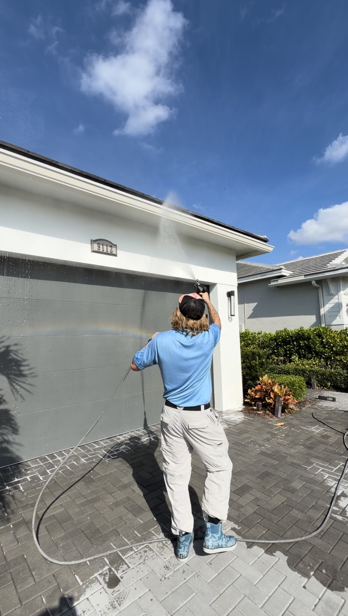 Person pressure washing the garage door of a house on a sunny day.
