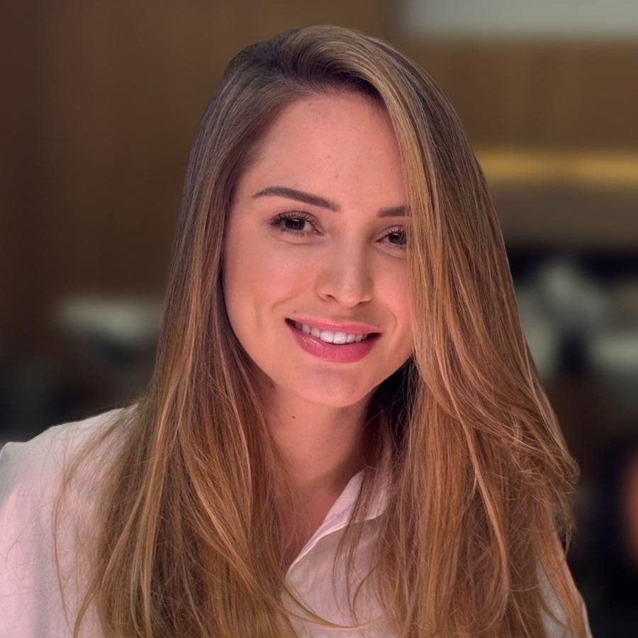 Portrait of a young woman with long, light brown hair, smiling, wearing a white shirt, in an indoor setting.