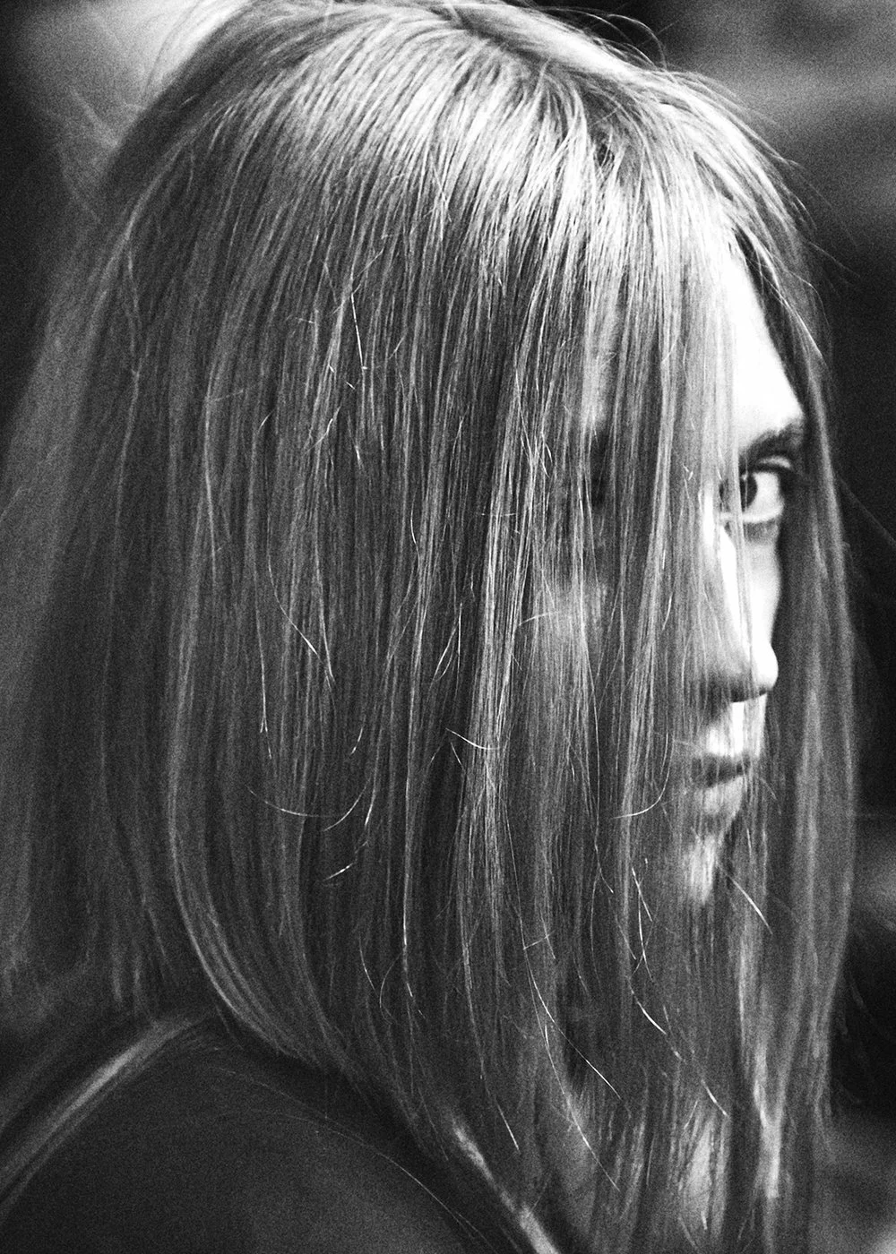 Side profile of a woman with long, straight hair and partially visible face, looking over her shoulder, in black and white.