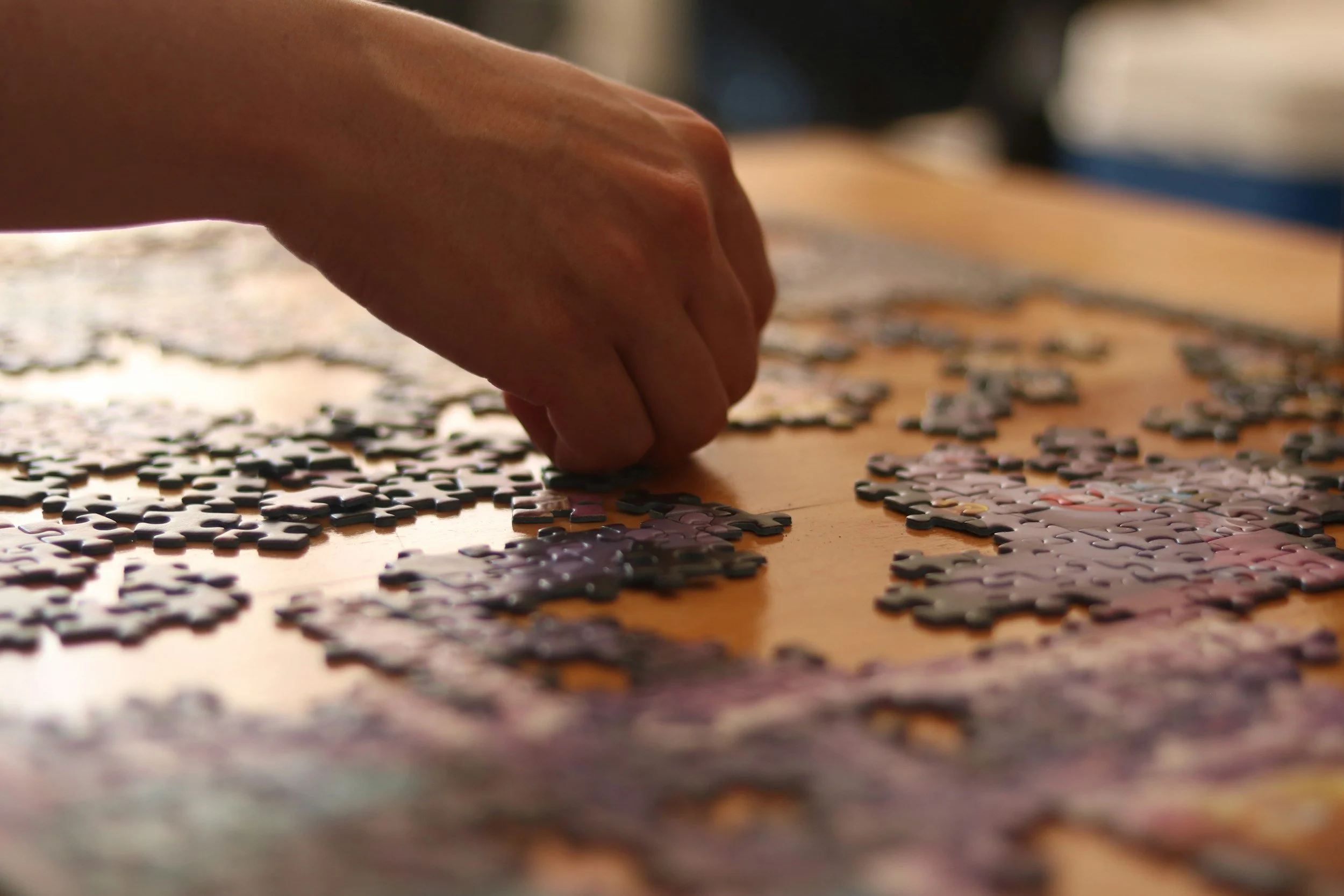 A hand assembling jigsaw puzzle pieces on a wooden table.