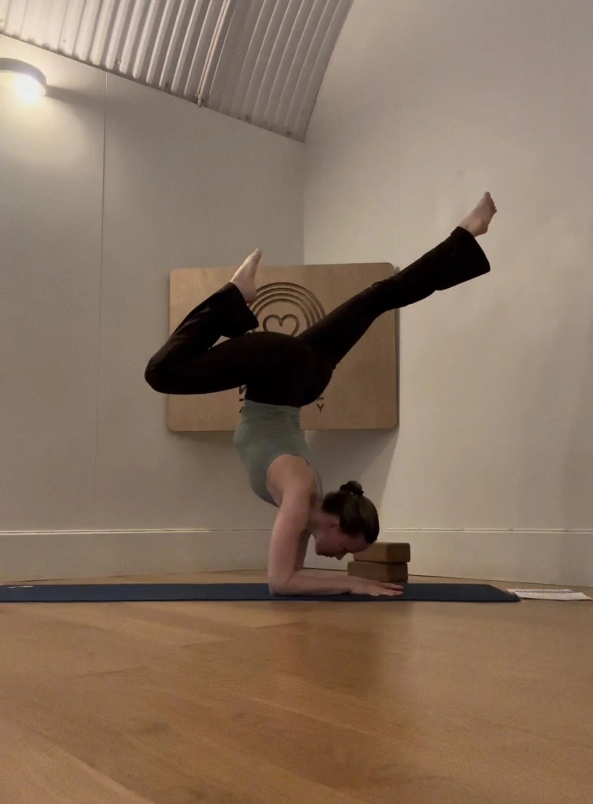 A woman practicing yoga in a headstand pose on a yoga mat indoors.