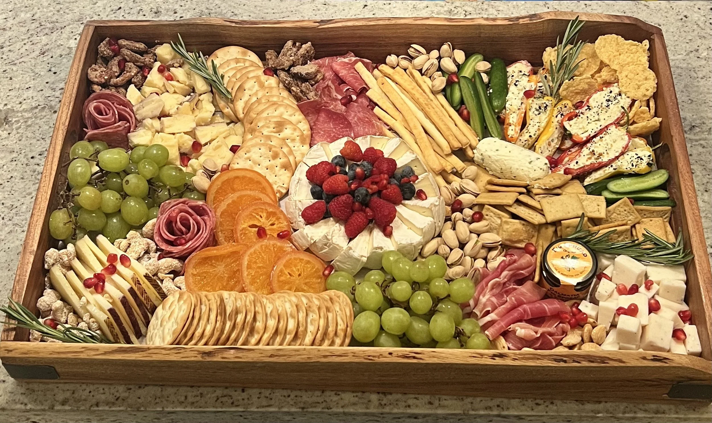 A wooden charcuterie board with cheeses, fruits, crackers, nuts, cured meats, and various garnishes arranged in an elegant presentation created by Cannon's Table.