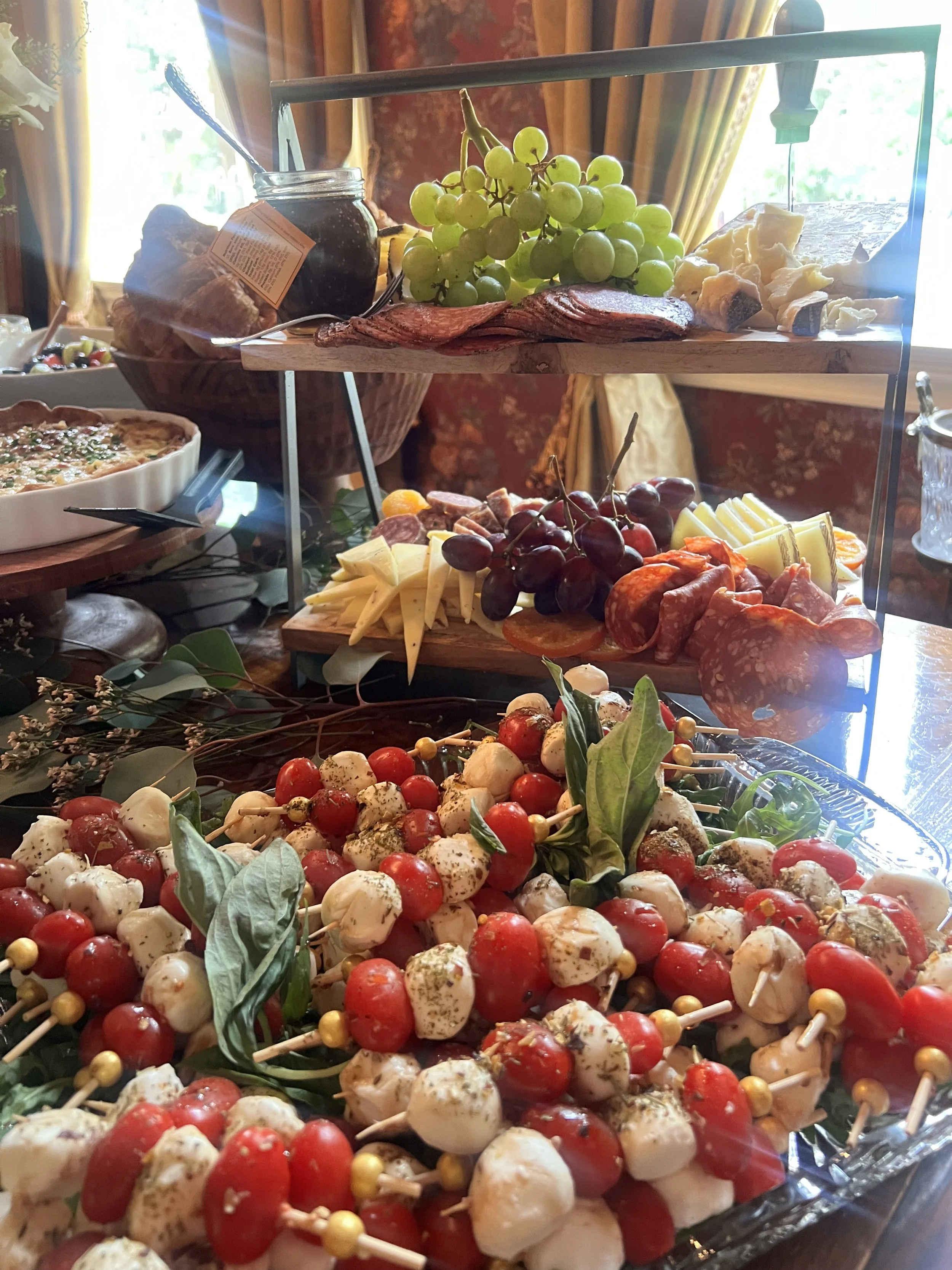 A grazing table including cheese and fruit platter featuring grape clusters, cherry tomatoes, mozzarella, with a charcuterie section created by Cannon's Table.