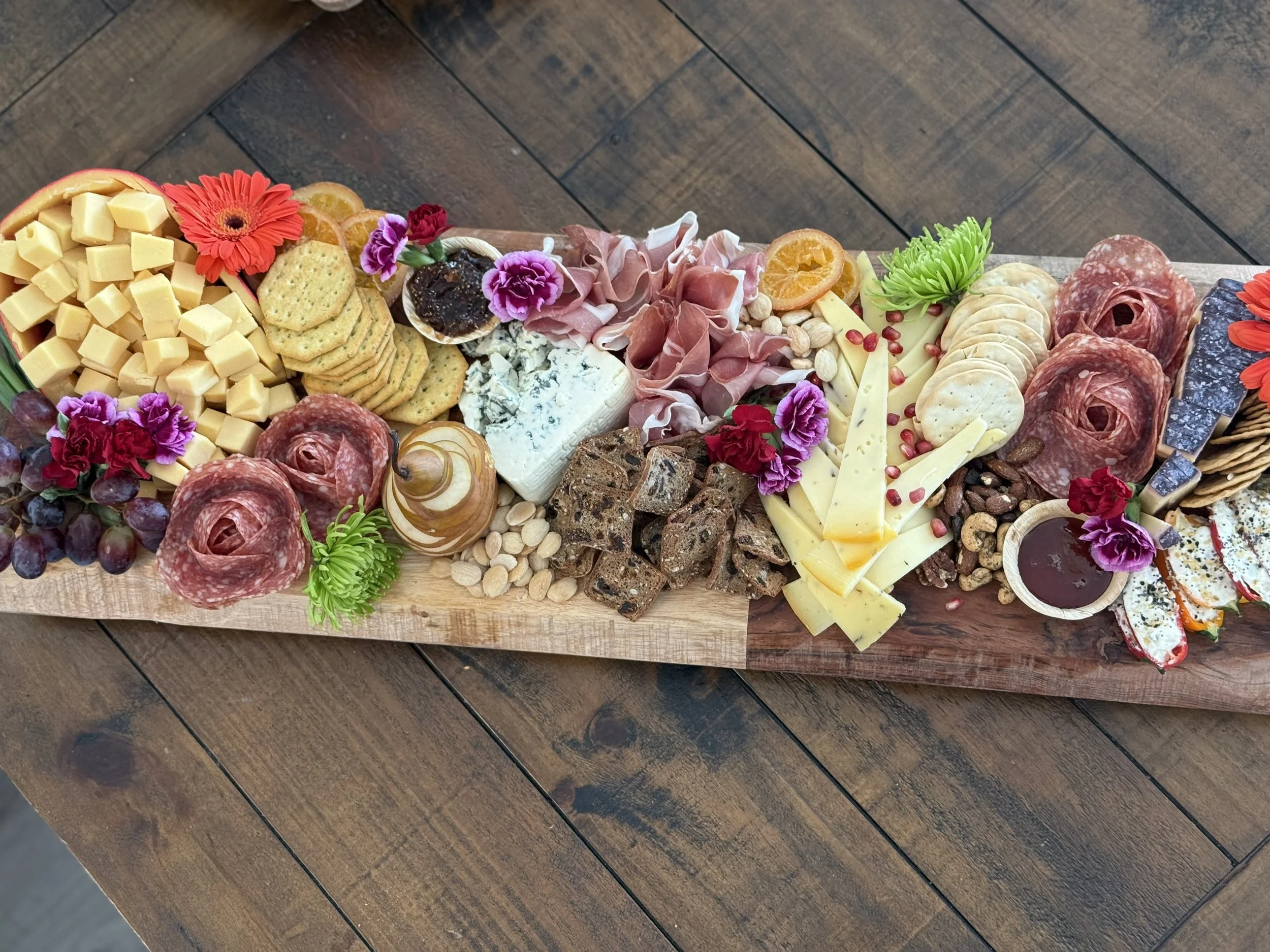 Charcuterie board with cheese, meats, crackers, grapes, dried fruit, nuts, and edible flowers on a wooden table created by Cannon's Table.