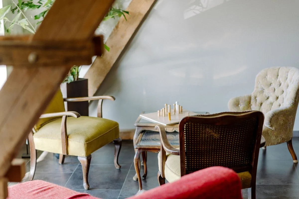 Das Bild zeigt einen Zimmerausschnitt mit drei antiken Sesseln und in deren Mitte einen kleinen Tisch. Darauf steht ein Holzbrett mit Holzfiguren, das man für die Aufstellungsarbeit benutzt.