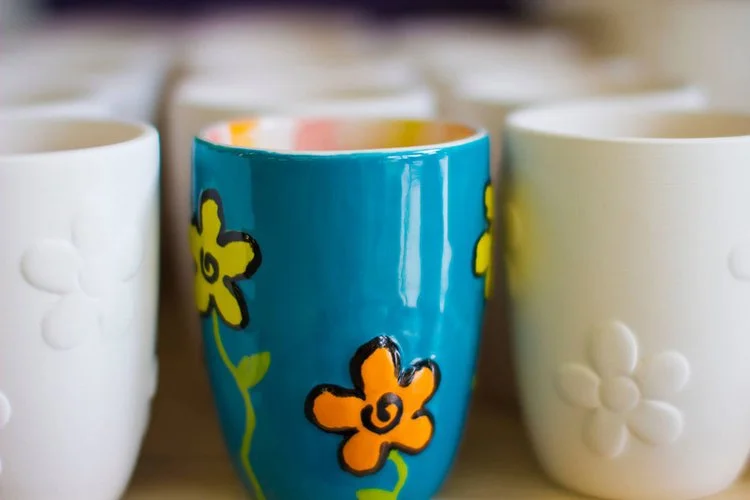 Colorful ceramic mugs with flower designs arranged on a shelf.