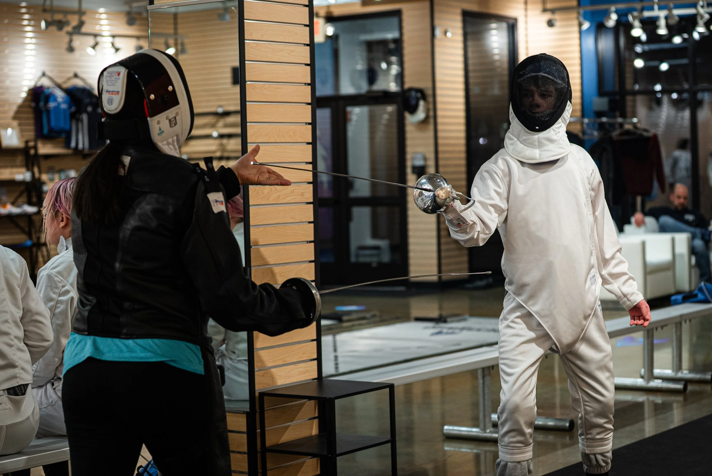 Two fencers in fencing gear exchanging touches at an indoor fencing event.