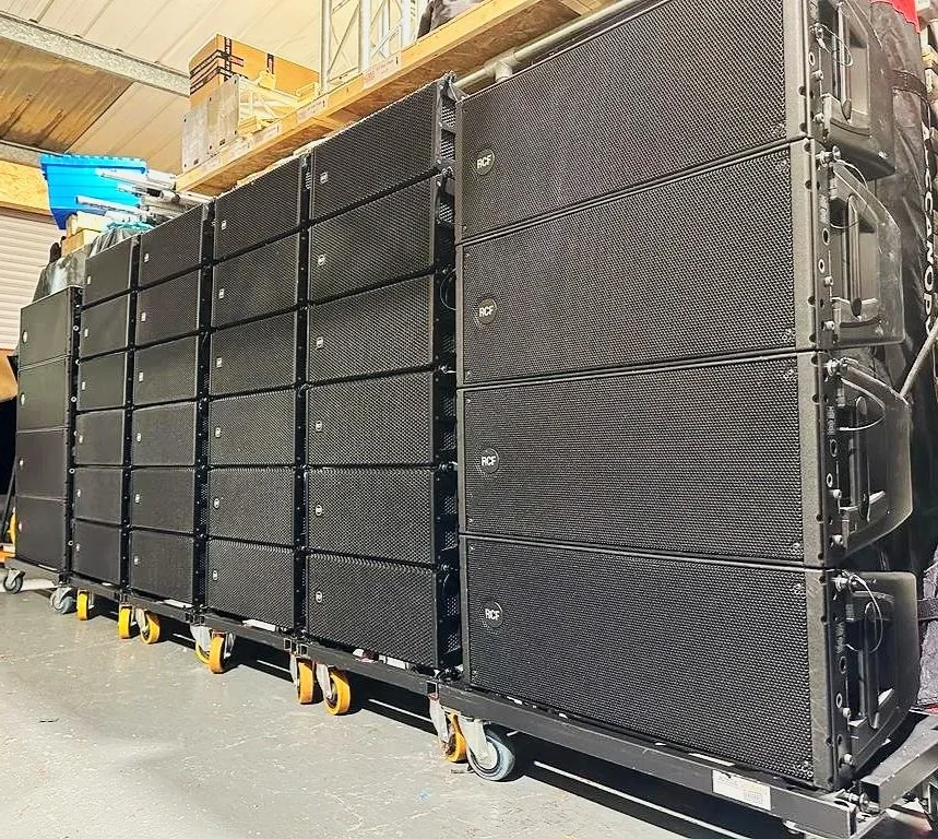 A large line array speaker system set up in a warehouse or storage area, supported on a wheeled trolley.