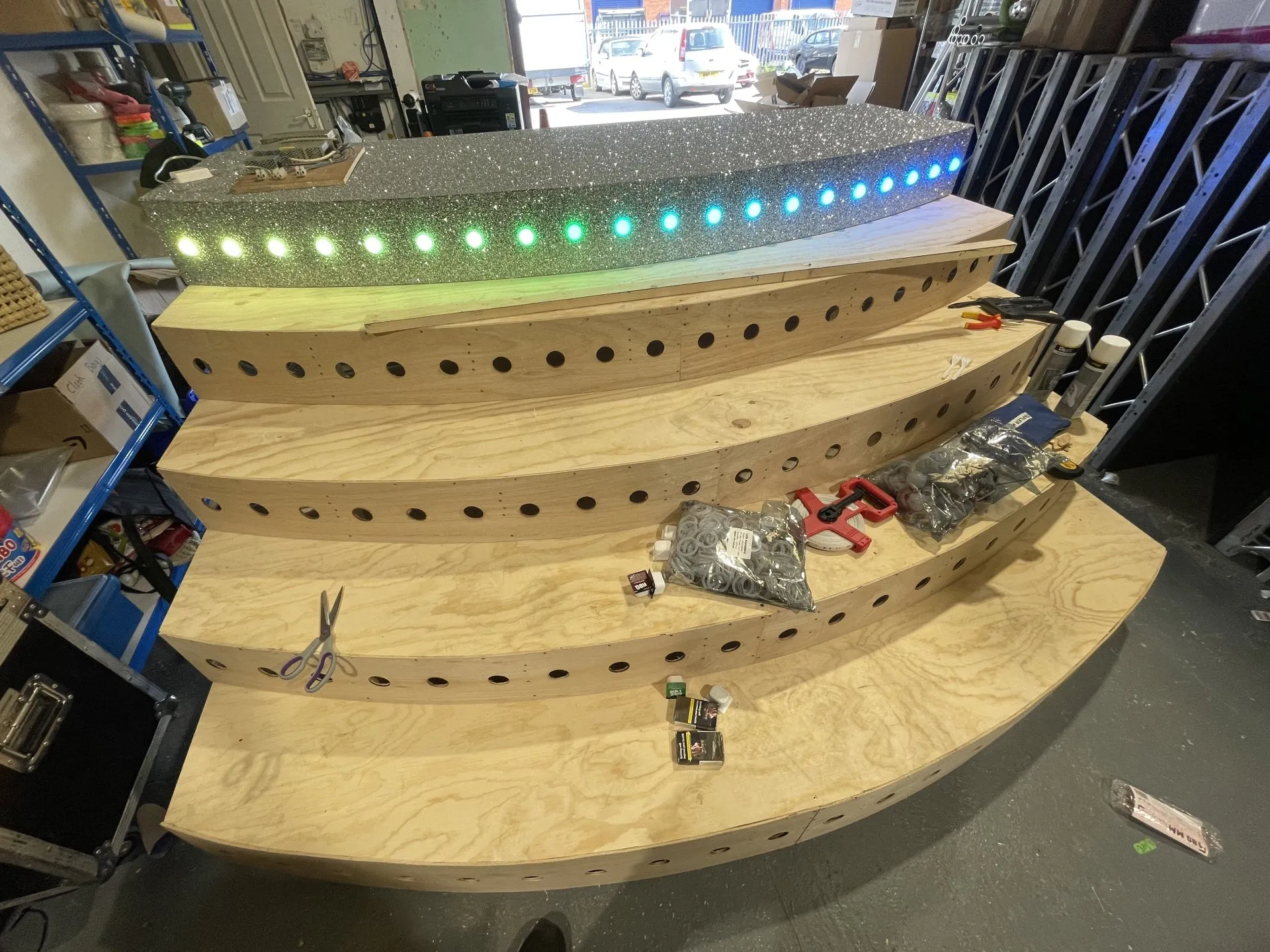 Wooden steps with hole patterns being assembled in a workshop, with LED lights and tools on the steps.