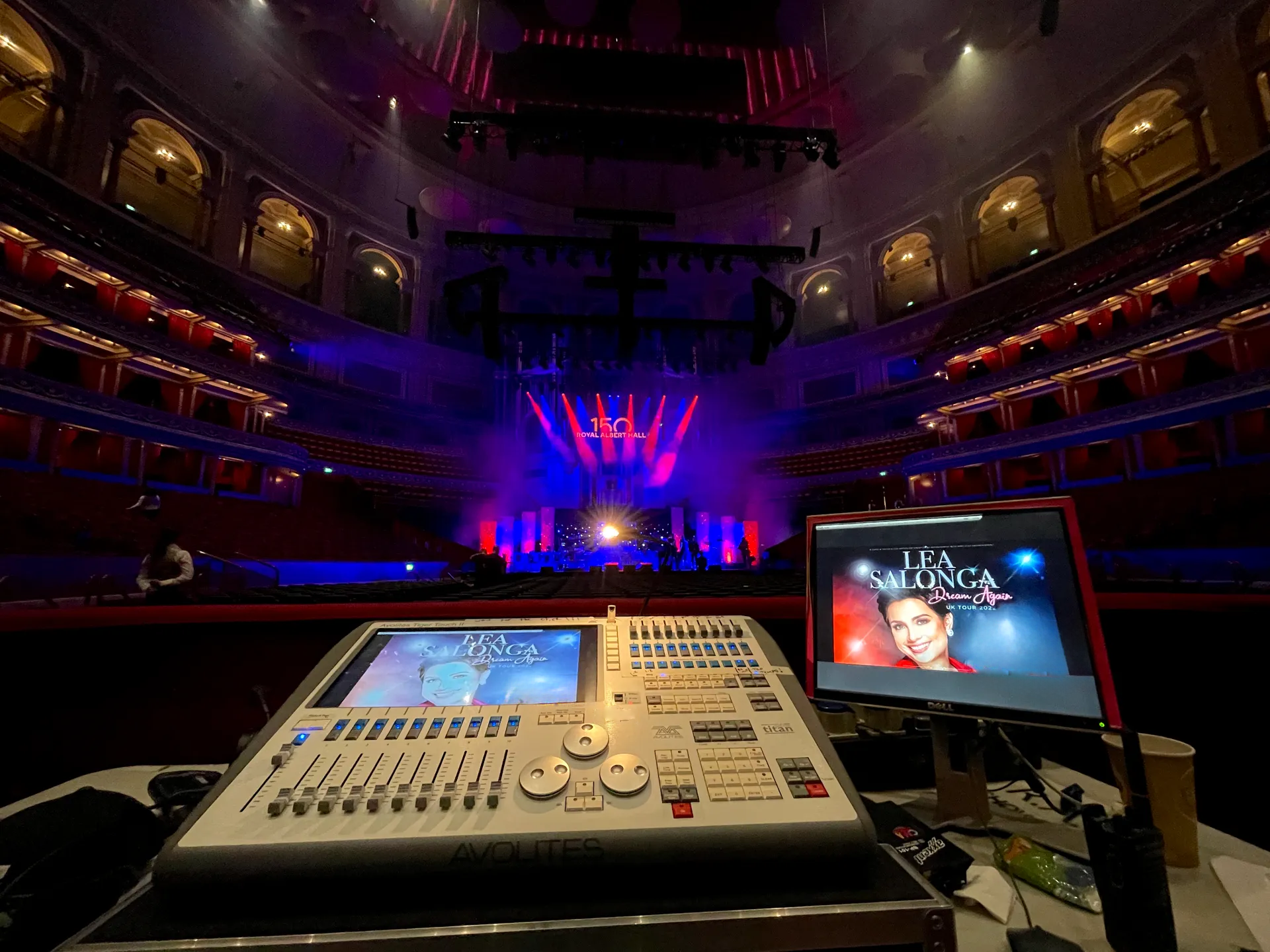 A concert stage in a large theatre with lighting and sound equipment set up. Two monitors display promotional graphics for Lea Salonga's Dream Again tour. The theater's interior features multiple balcony levels.