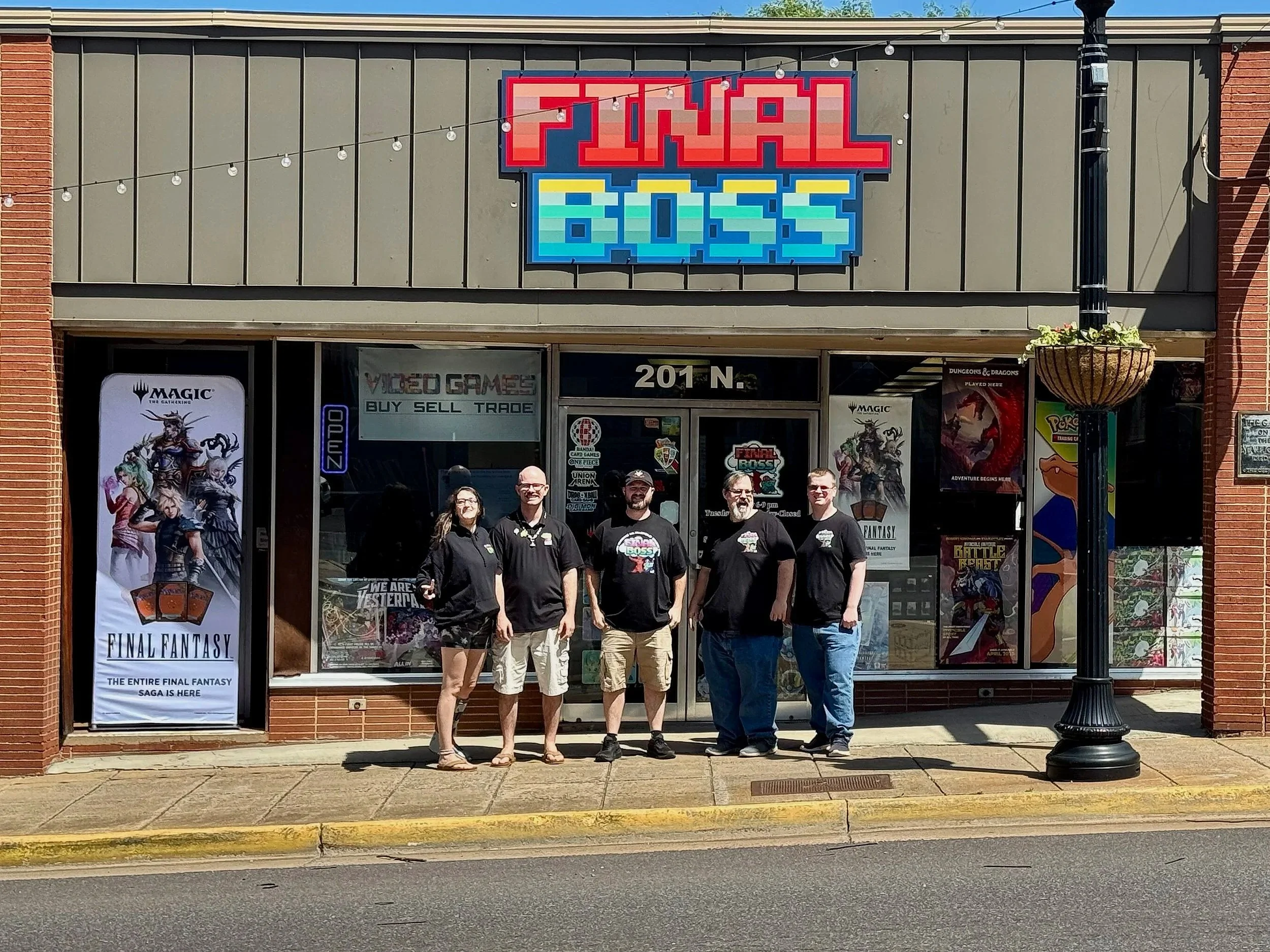 Group of five store employees standing outside video game store with store sign and posters.