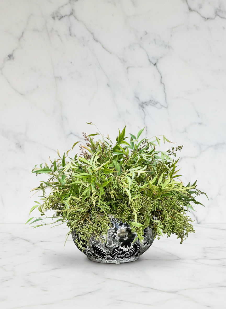 A decorative black and white ceramic bowl filled with various green leafy plants, set on a white marble surface with a marble wall in the background.