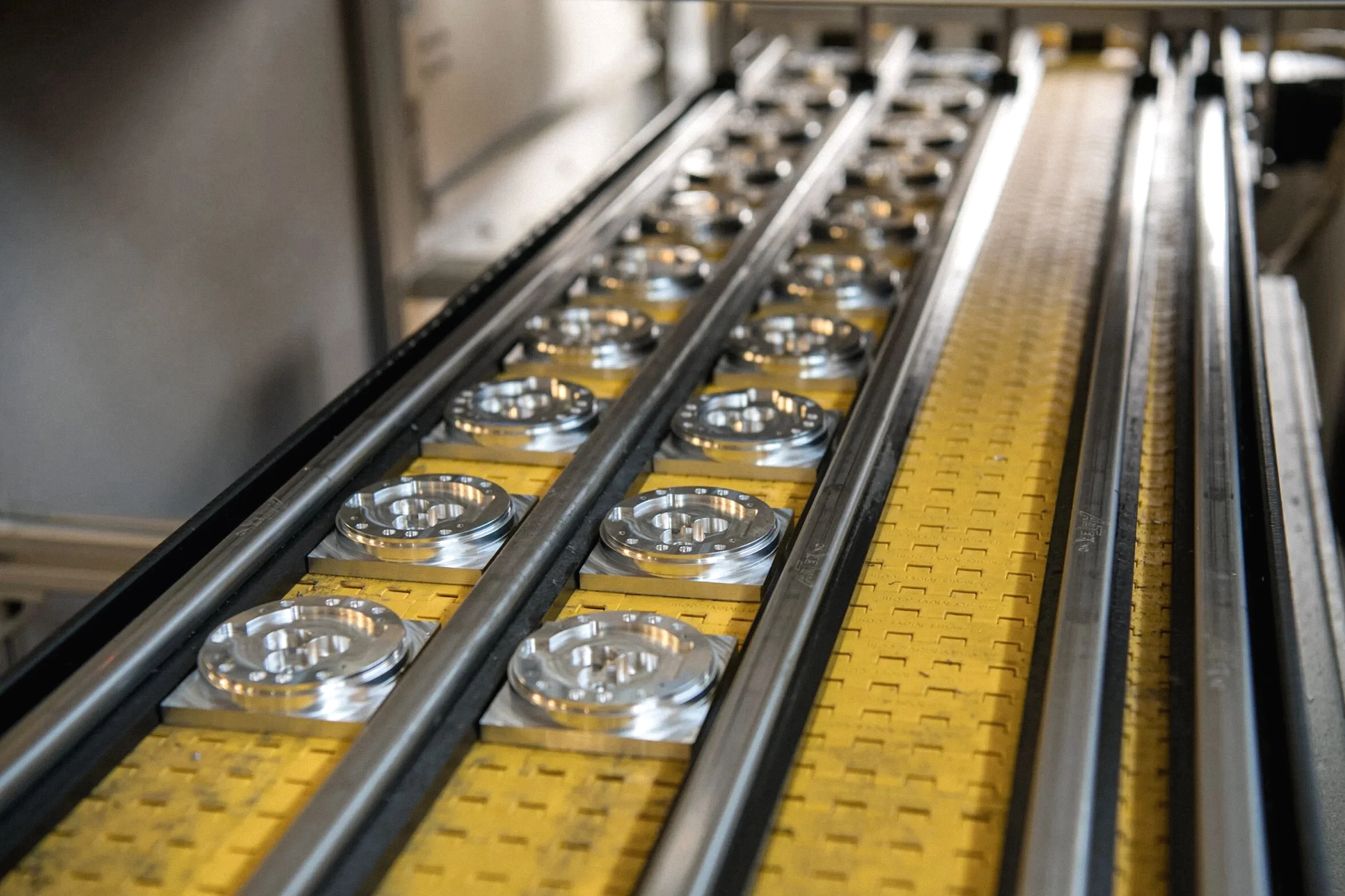 Close-up of a conveyor system transporting shiny metal components on yellow rollers in a manufacturing or industrial setting.
