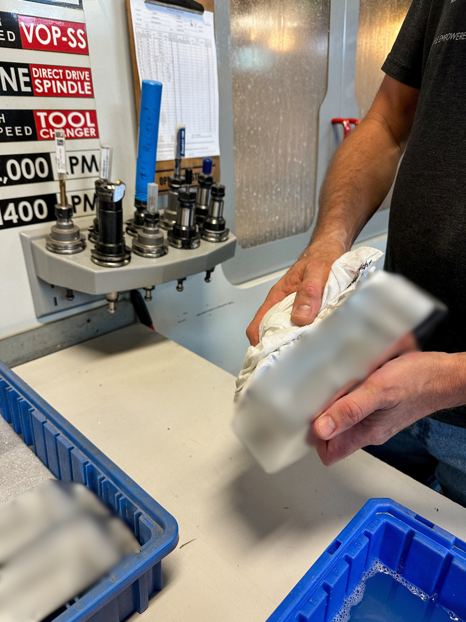 A person holding a mission-critical part blurred up for privacy reasons, with various tool parts and equipment on the workbench in the background.