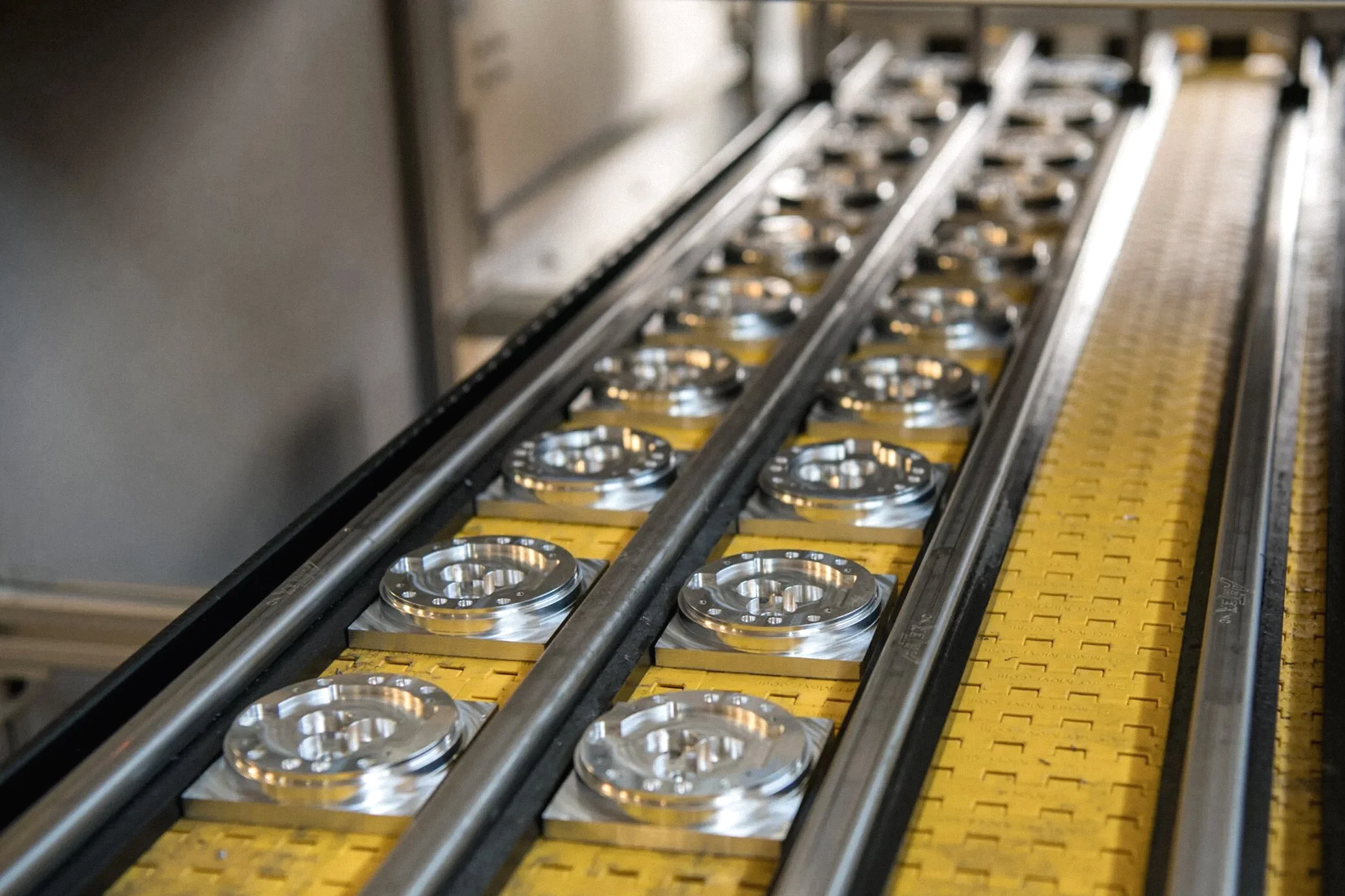 A conveyor system with circular metallic parts on a yellow and black conveyor belt in an industrial setting.