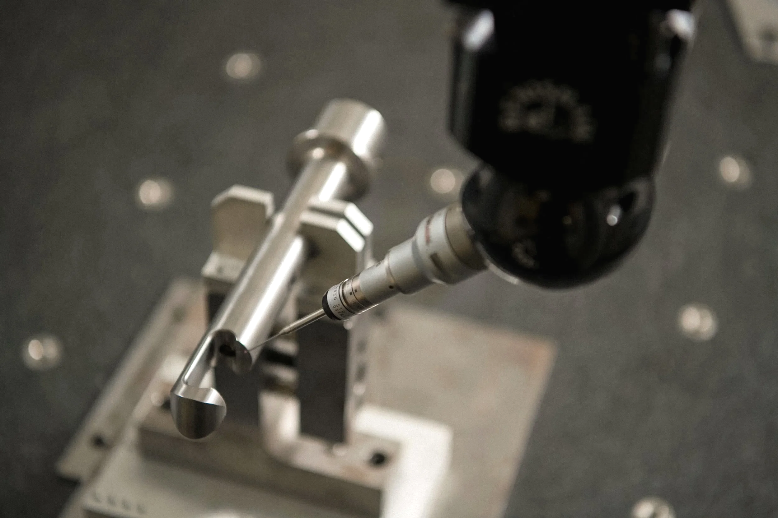 Close-up of a robotic arm with a precision instrument attached to it, mounted on a white base, on a dark speckled surface.