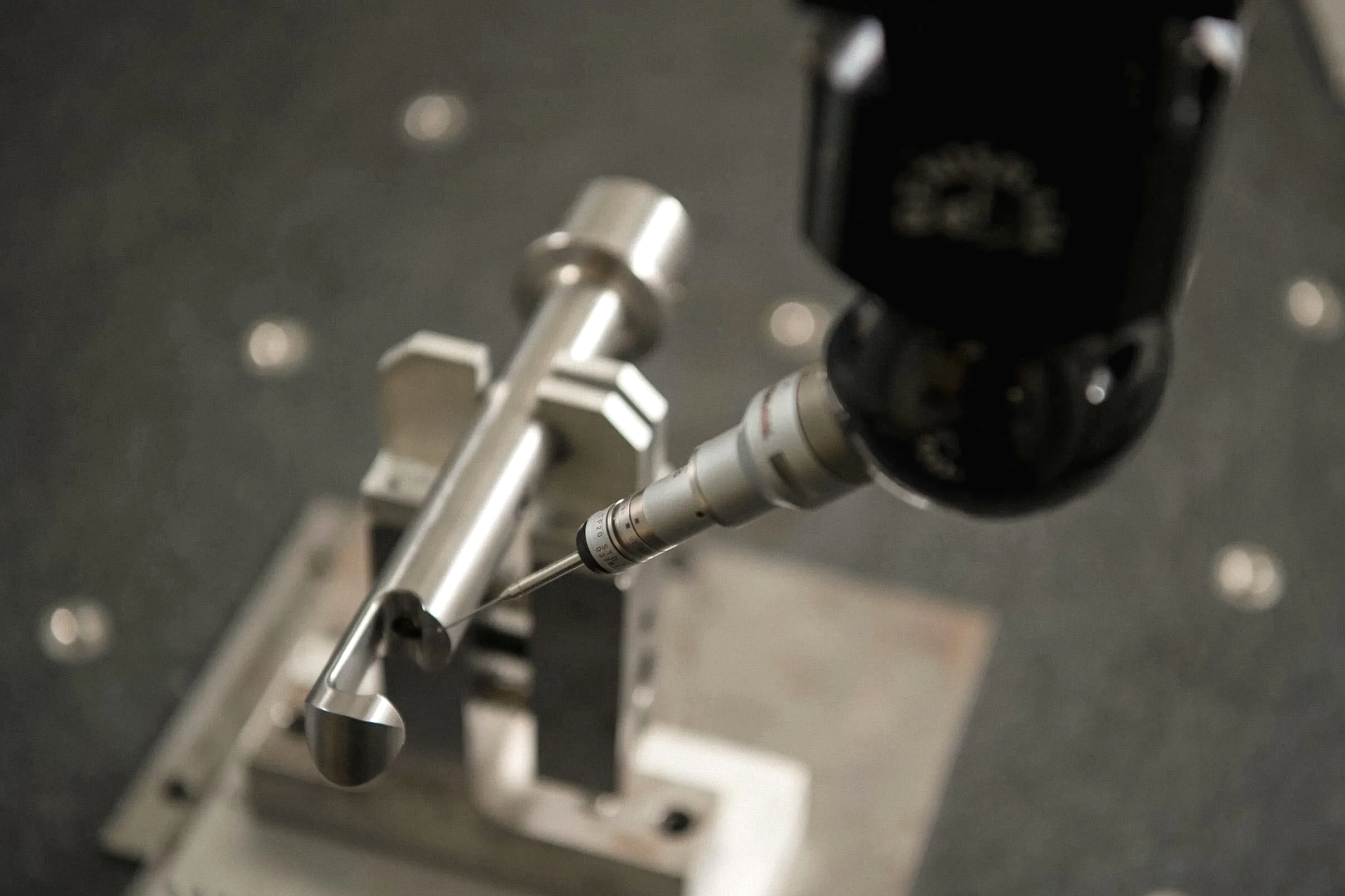 Close-up of a scientific instrument or piece of equipment with a metal component and a black attachment, set on a metallic surface with scattered circular and rectangular features.