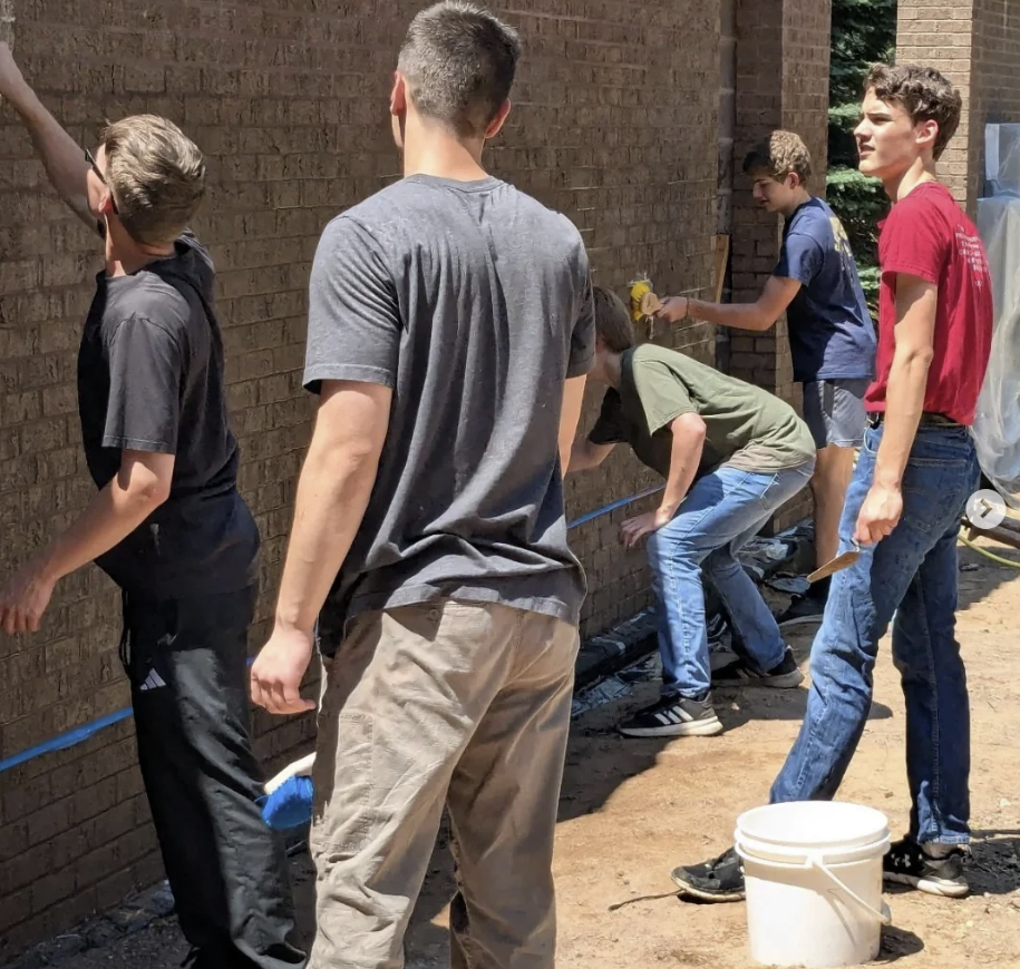 A group of young boys working together to paint or do construction on a brick wall outside.