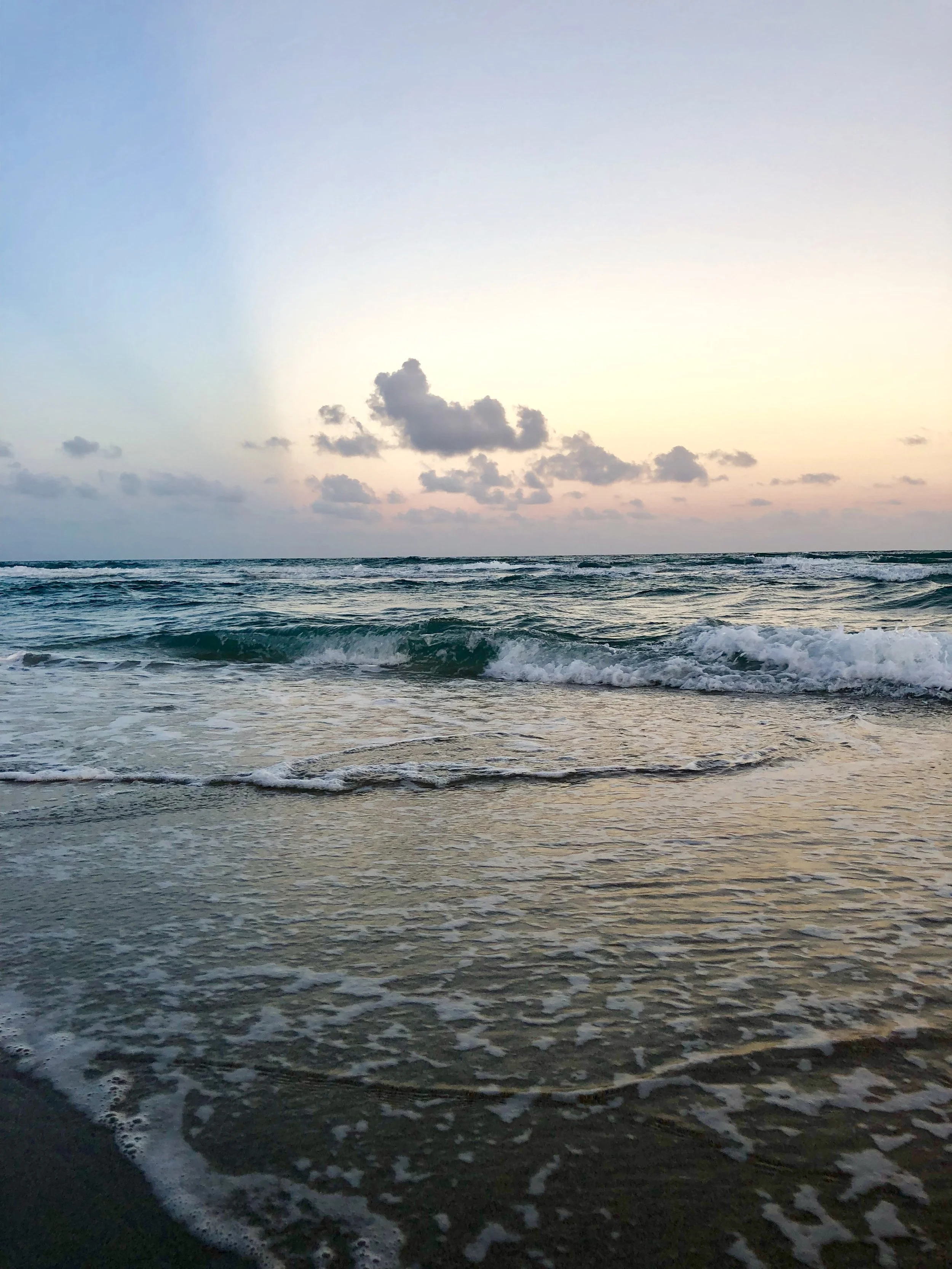 Sunset over the ocean with gentle waves and cloudy sky.