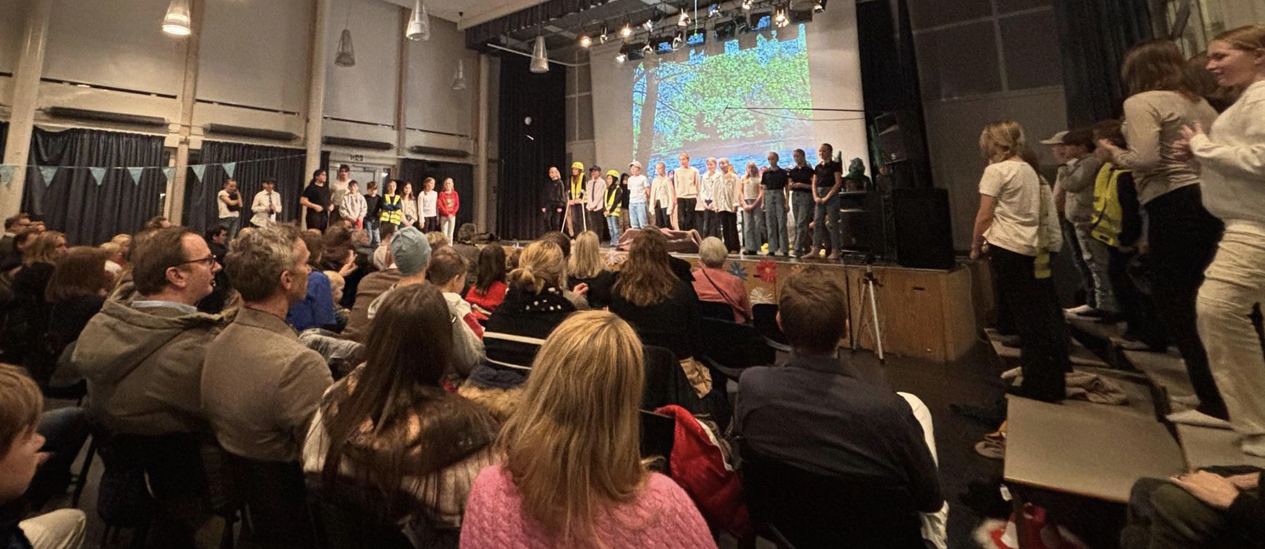 En gruppe mennesker oppfører seg på en scene foran et publikum i en teatersal.