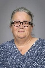 Portrett av en eldre kvinne med briller, grått hår og en blå sweater