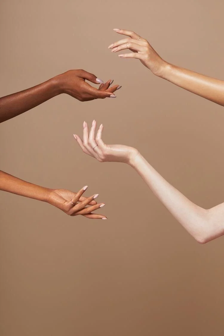 Four hands reaching out towards each other against a beige background, with some hands wearing rings and having different skin tones.