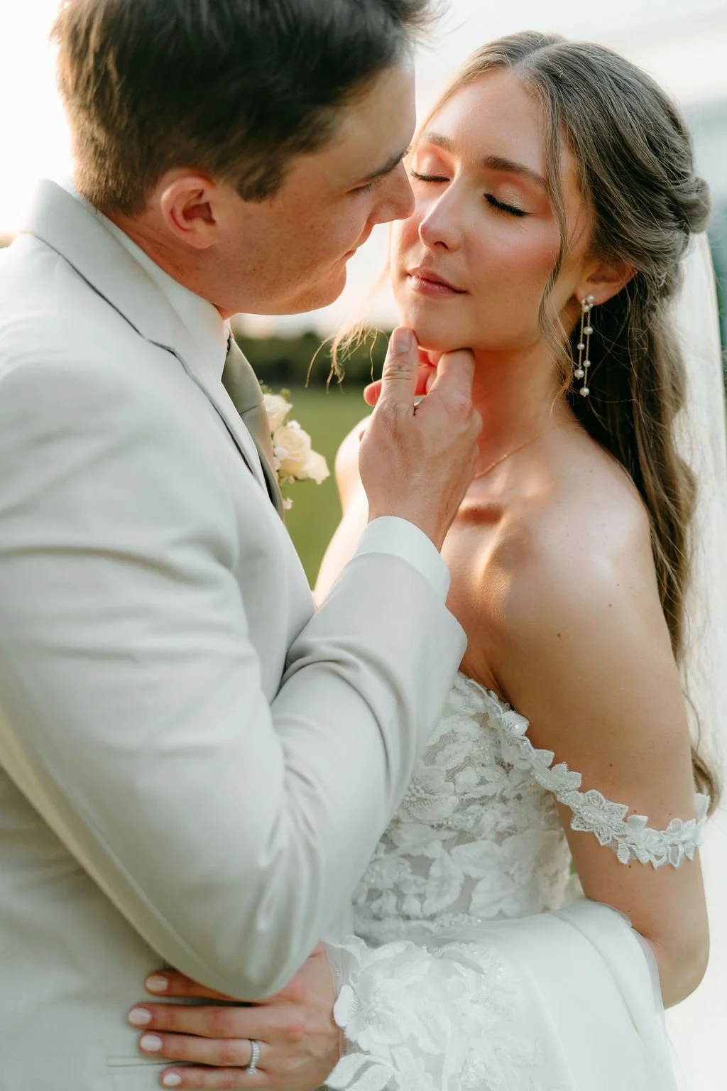 A couple sharing a kiss on their wedding day, with the groom gently holding the bride's face and neck.