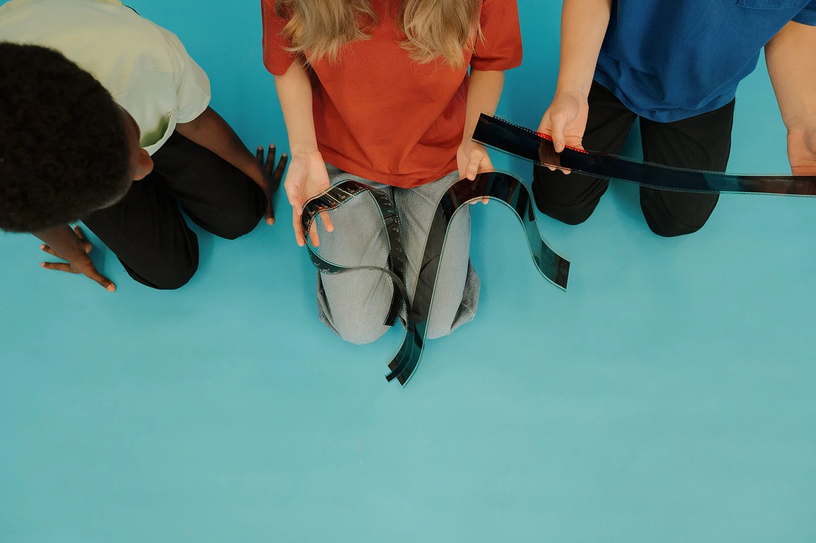 From above, looking down on three kids looking at celluloid film strips on their laps