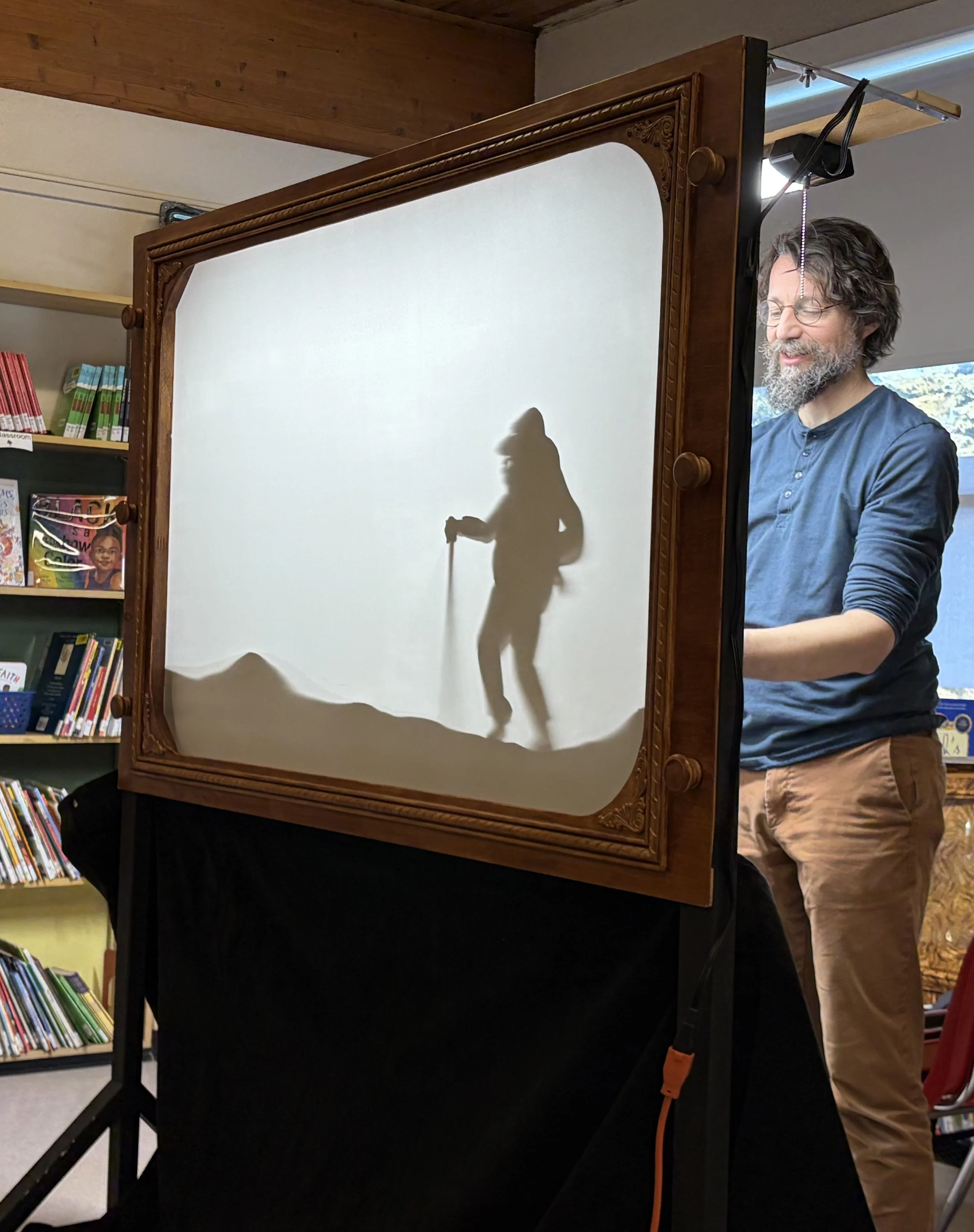 Filmmaker Curtis Wiebe demonstrating shadow puppets behind a screen
