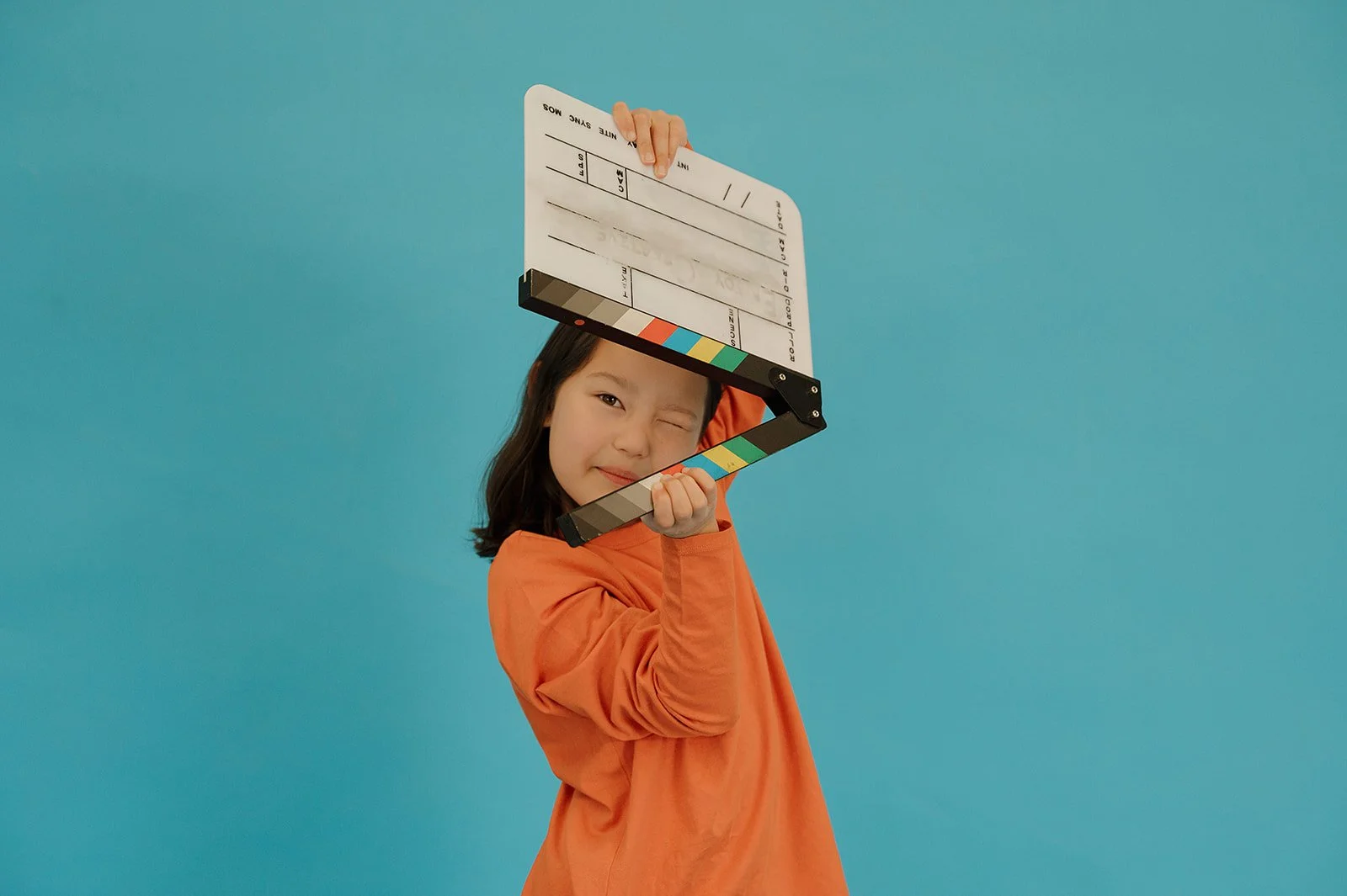 A girl with one eye closed looking through the arms of an upside down film clapper