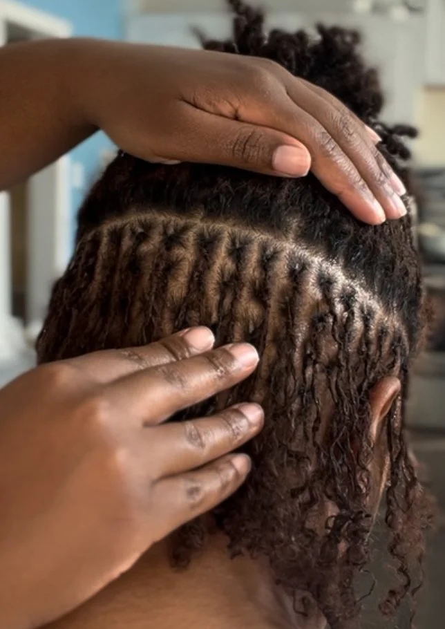 Person during microlock retightening session, hair sectioned to show individual twists or locs.