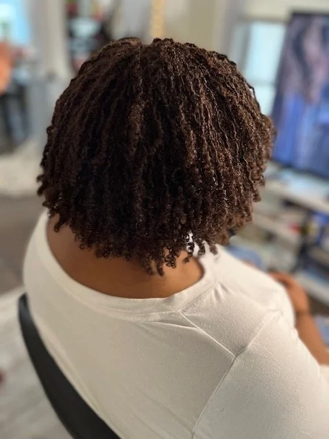 Back of person with natural dark curly hair sitting in a room.