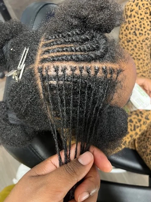 Close-up of a person's natural hair with sections prepared for a protective style, including braids and twists.