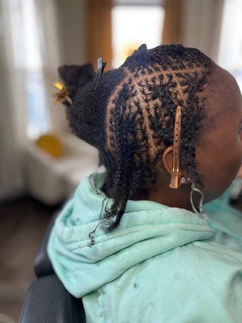 Close-up of a person's natural hair with sections prepared for a protective style, including braids and twists.