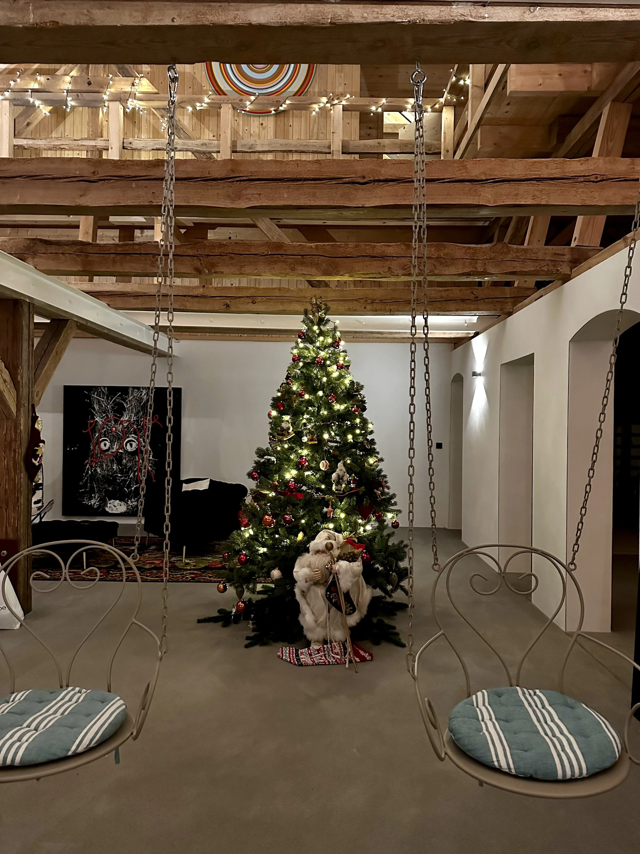 Weihnachtsbaum in einem Raum mit Holzdecken, geschmückt mit Lichtern, Kugeln und Ornamenten, mit einem Rentiergewand und einem Weihnachtsstrumpf davor. Zwei Schaukelstühle mit gepolsterten Sitzen sind im Vordergrund.
