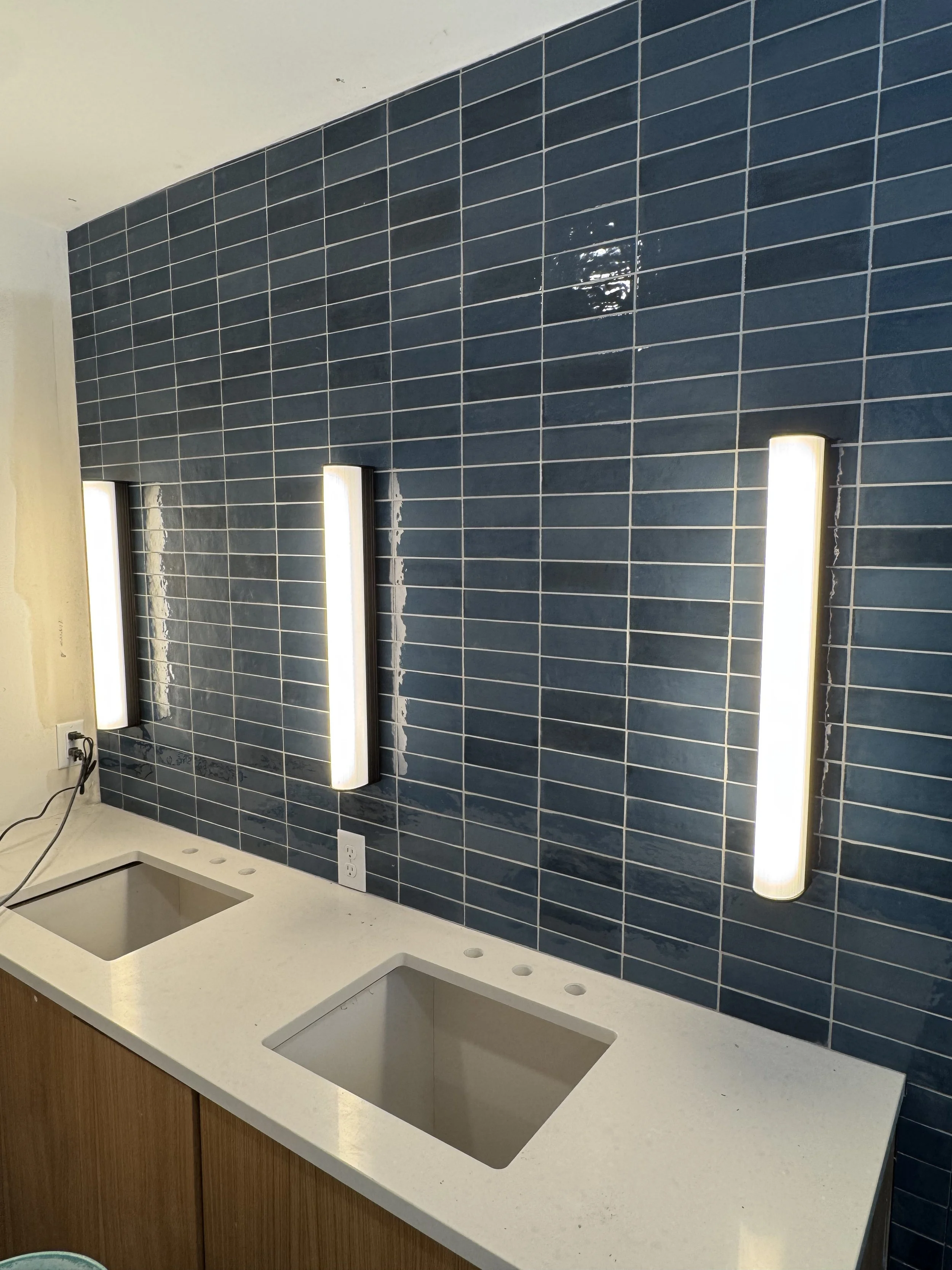 Bathroom vanity with two rectangular sinks, blue tiled wall, and three vertical light fixtures.