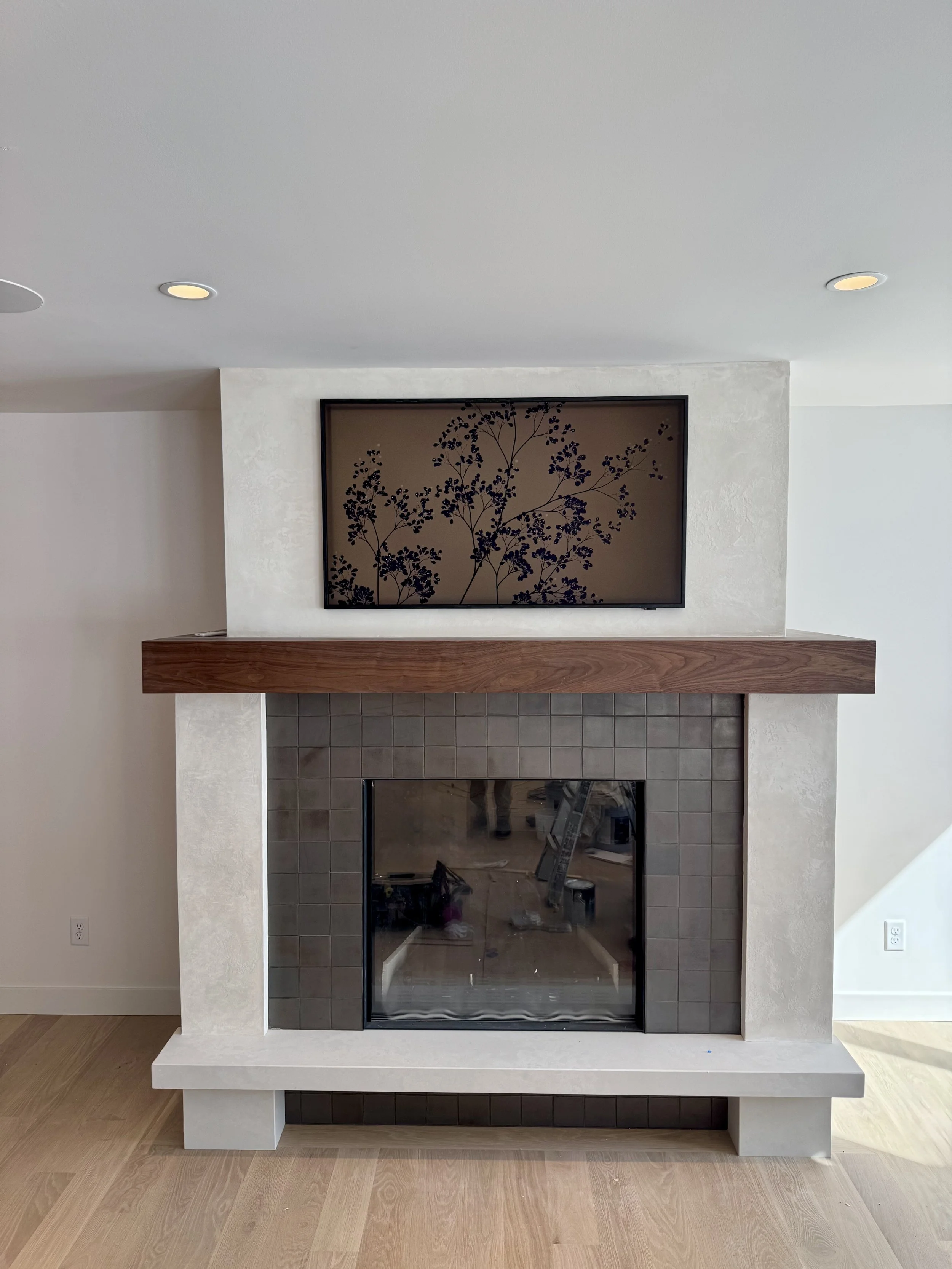 A modern fireplace with a wooden mantel and tiled surround, flat-screen TV above, and hardwood flooring in a contemporary living room.
