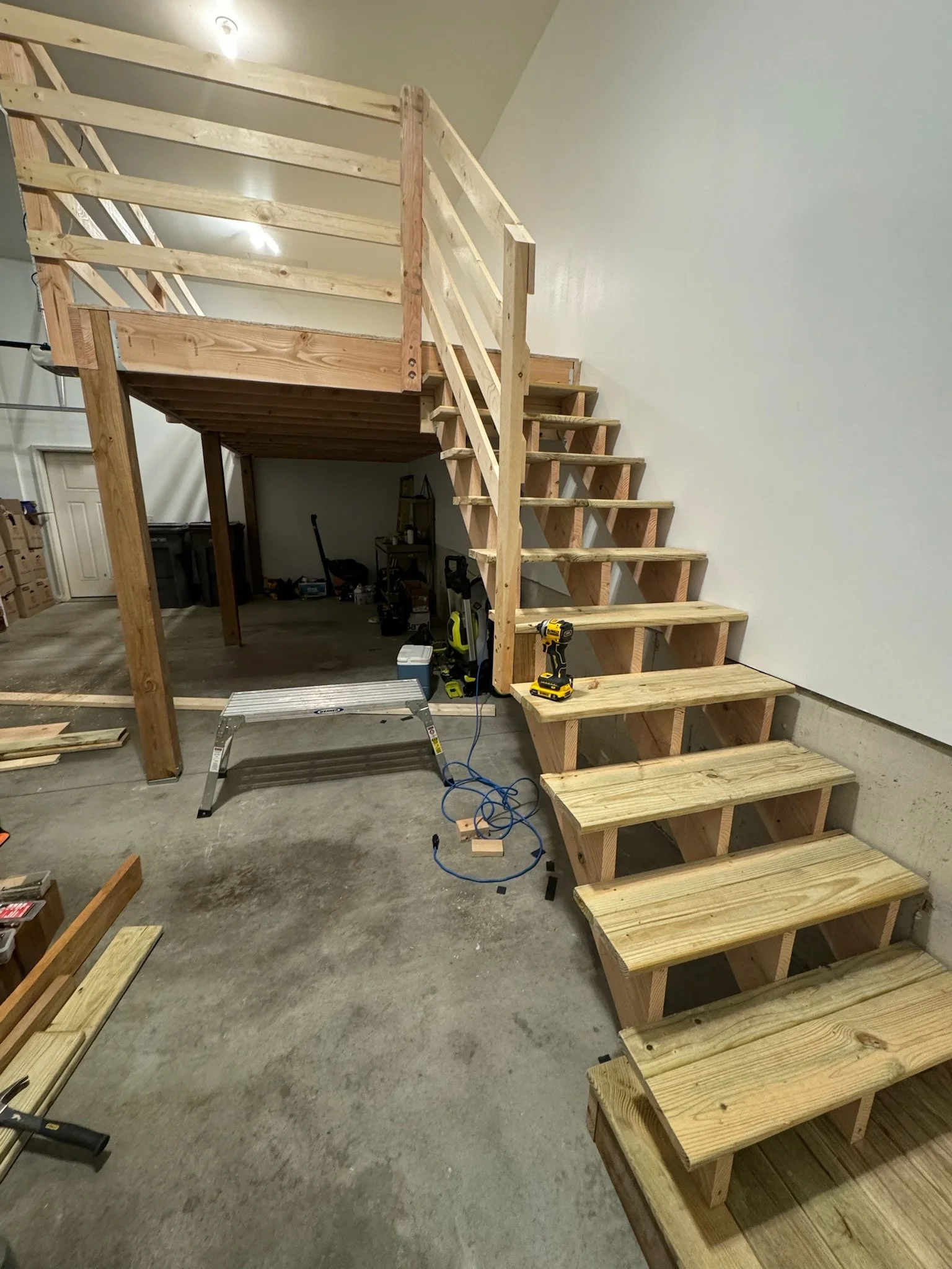 Wooden staircase construction inside a garage, with tools and building materials around.